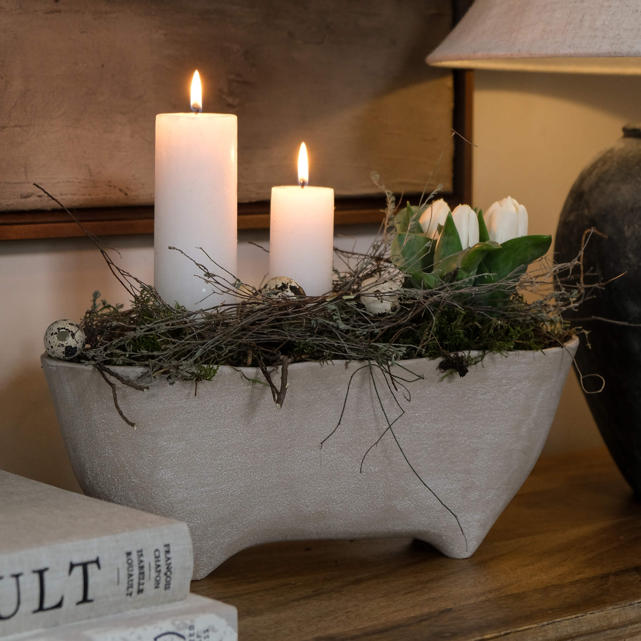 Centro de mesa de cerámica gris con velas blancas, ramas y tulipanes blancos sobre mesa de madera