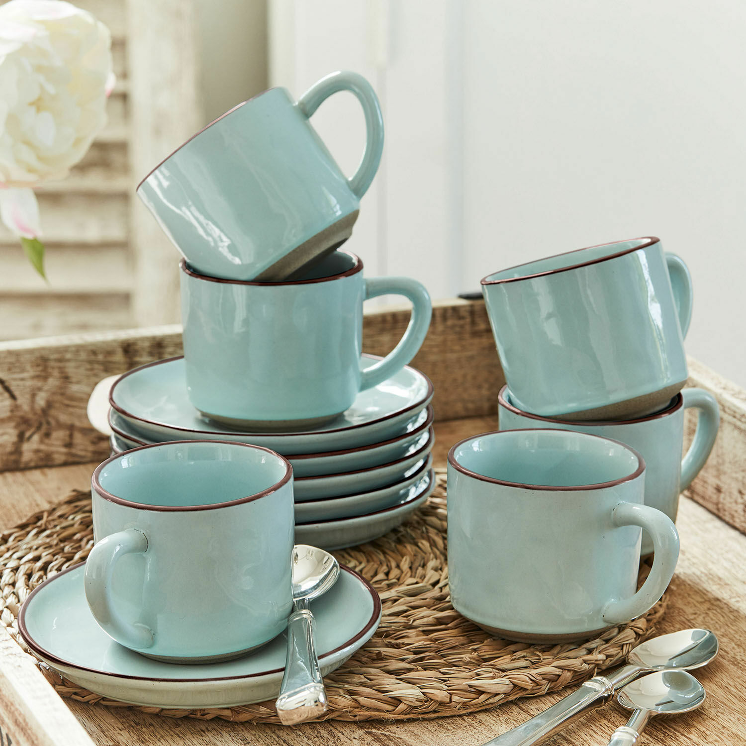 Set de 6 tazas y platillos Biarré Juego de tazas de cerámica azul claro con platos y cucharas sobre un posavasos trenzado
