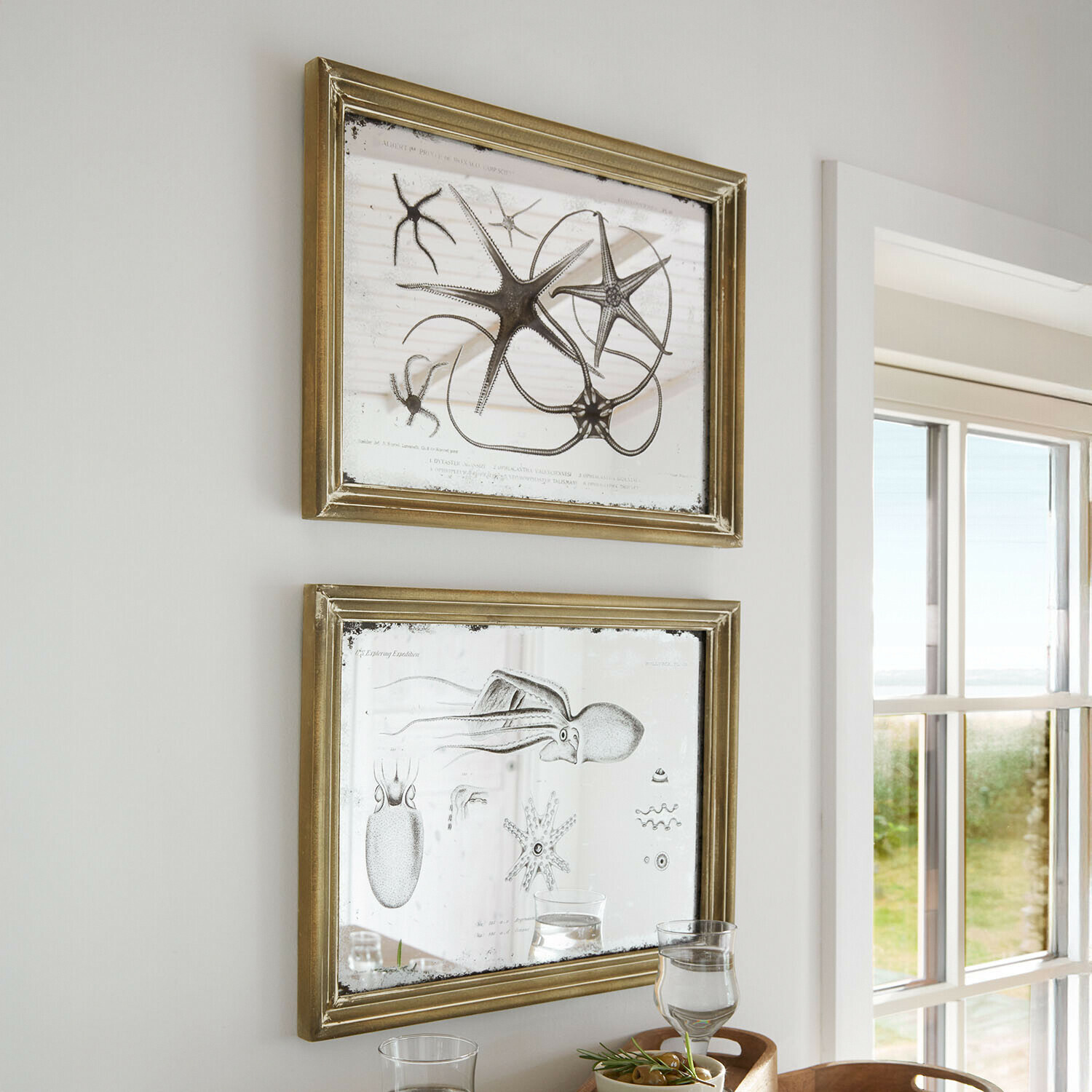 Dos marcos dorados con espejo e ilustraciones marinas, decoración de pared en habitación luminosa