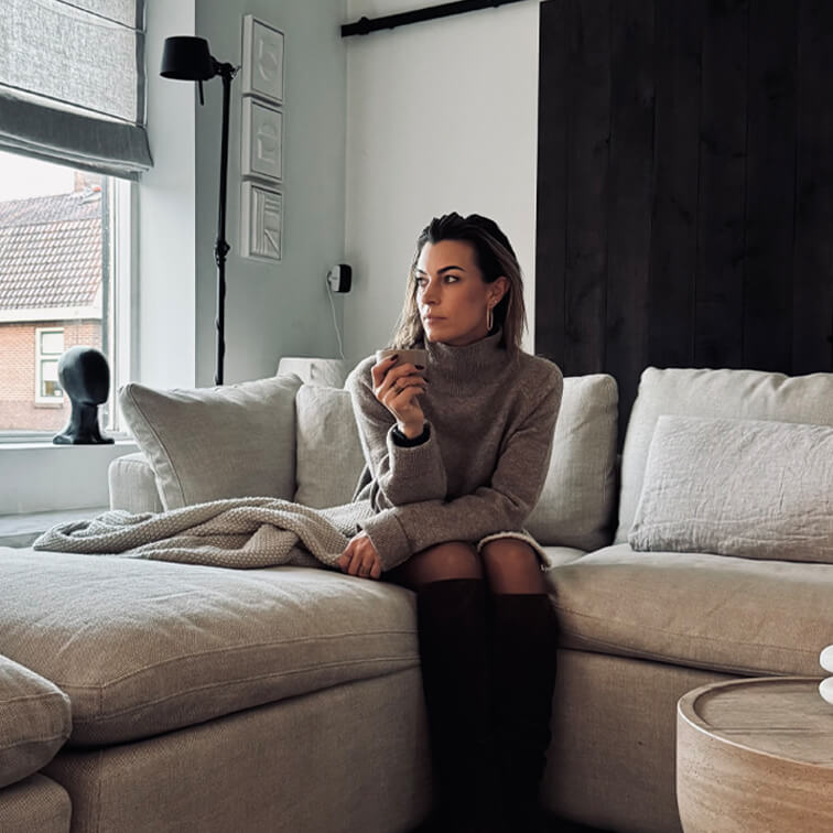 Mujer con suéter gris sentada en sofá beige en sala moderna con ventana grande