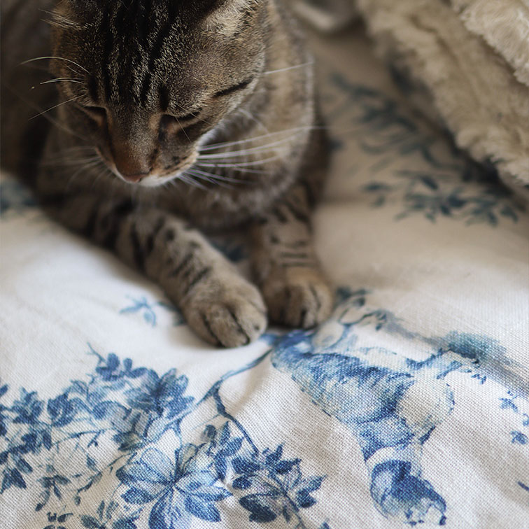 Gato atigrado gris sobre tela blanca con estampado floral azul, decoración suave para el hogar