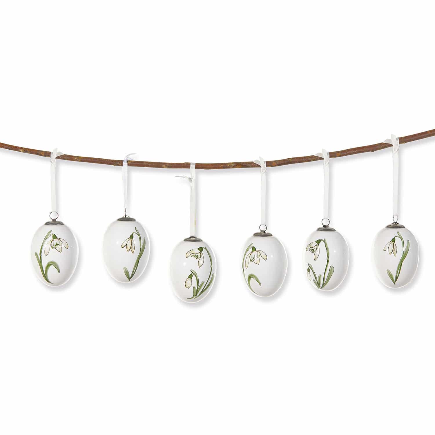 Conjunto de seis huevos de cerámica blanca con flores verdes colgados de una rama, decoración primaveral