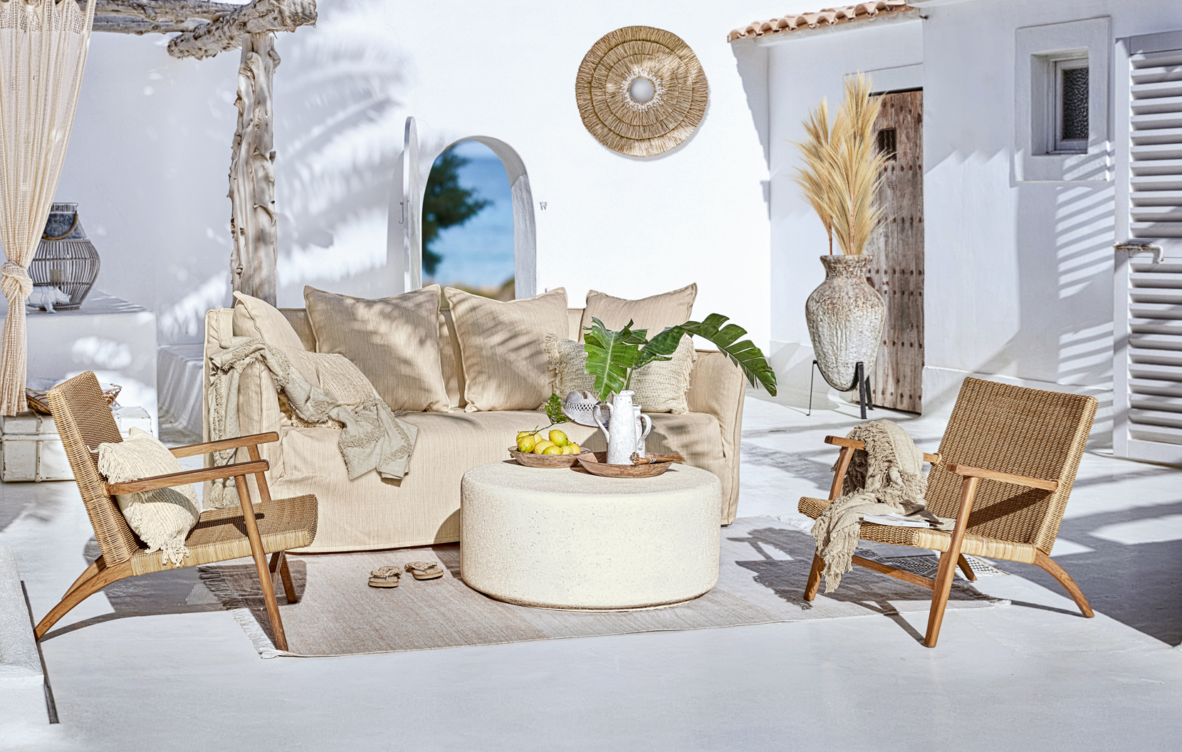 Conjunto de muebles de jardín bohemio con sofá beige y sillas de mimbre en terraza soleada