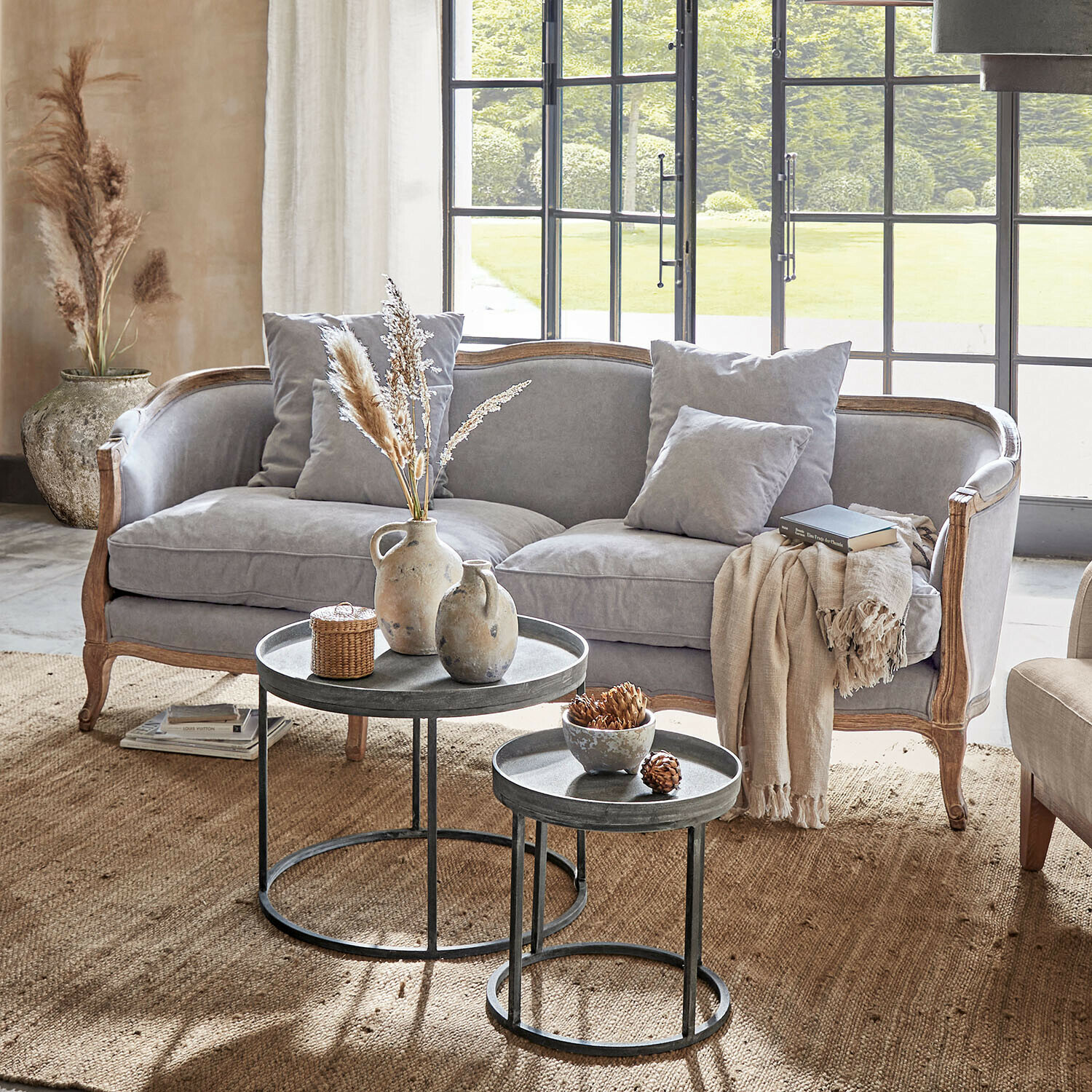 Sofa Monneville Sofá gris con marco de madera y cojines en sala luminosa con mesas de centro metálicas