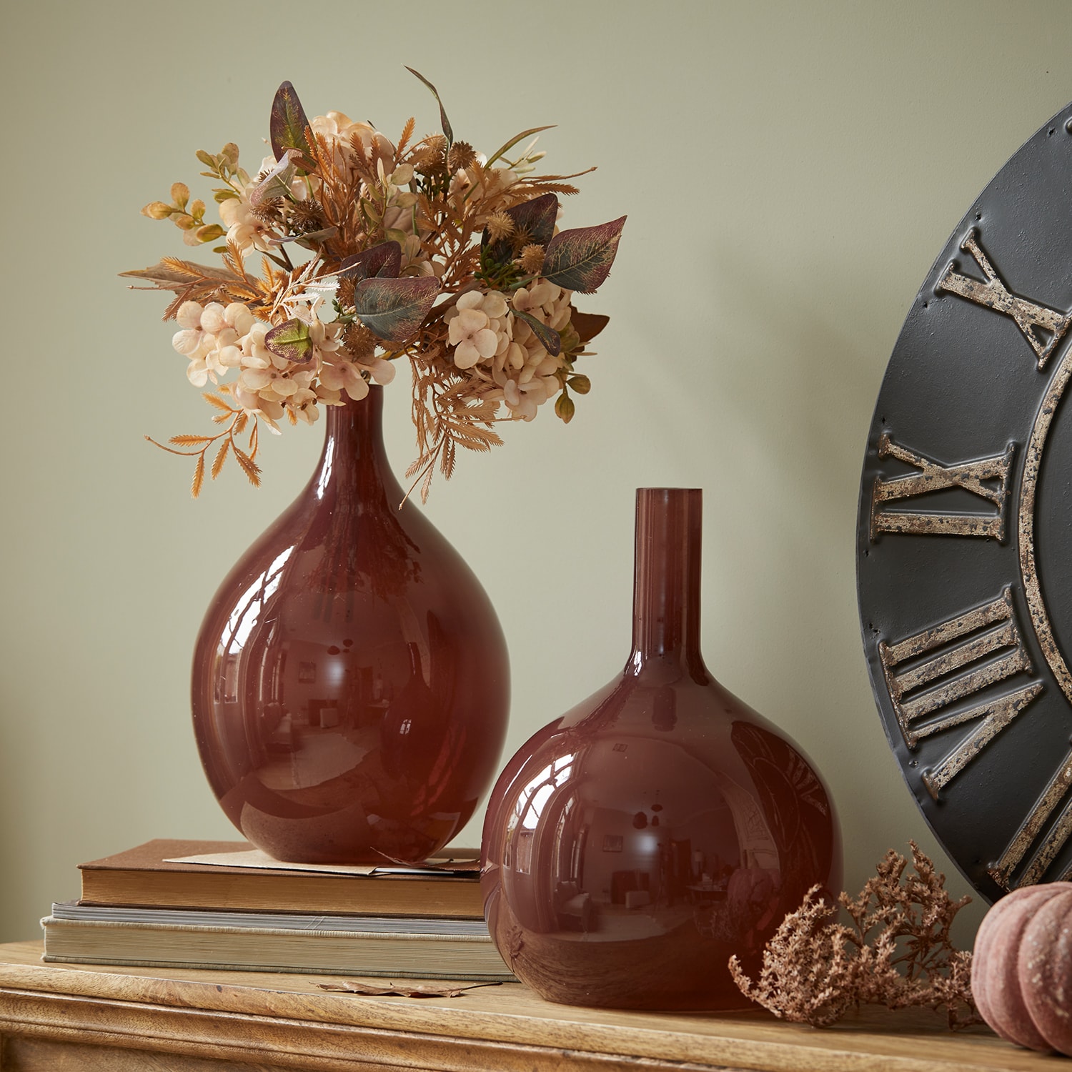 Dos jarrones decorativos de vidrio burdeos sobre mesa de madera con flores secas y libros
