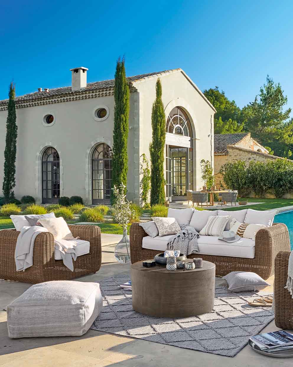 Conjunto de muebles de jardín de ratán marrón con cojines claros en terraza junto a piscina