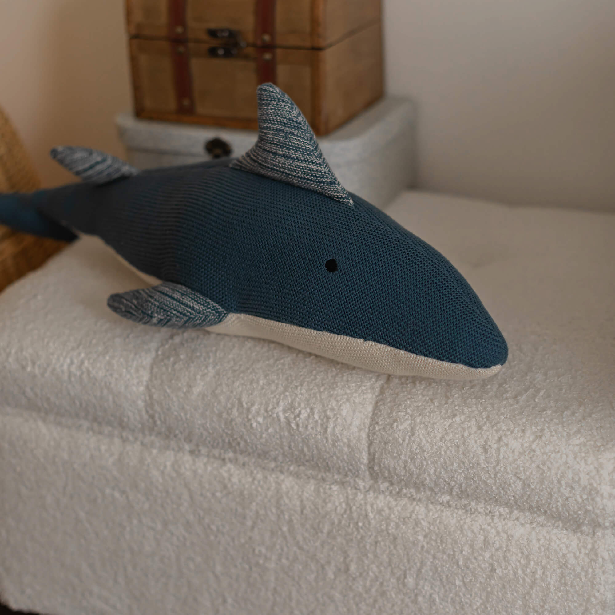 Cojín tejido azul marino con forma de tiburón sobre tela blanca suave, decoración infantil