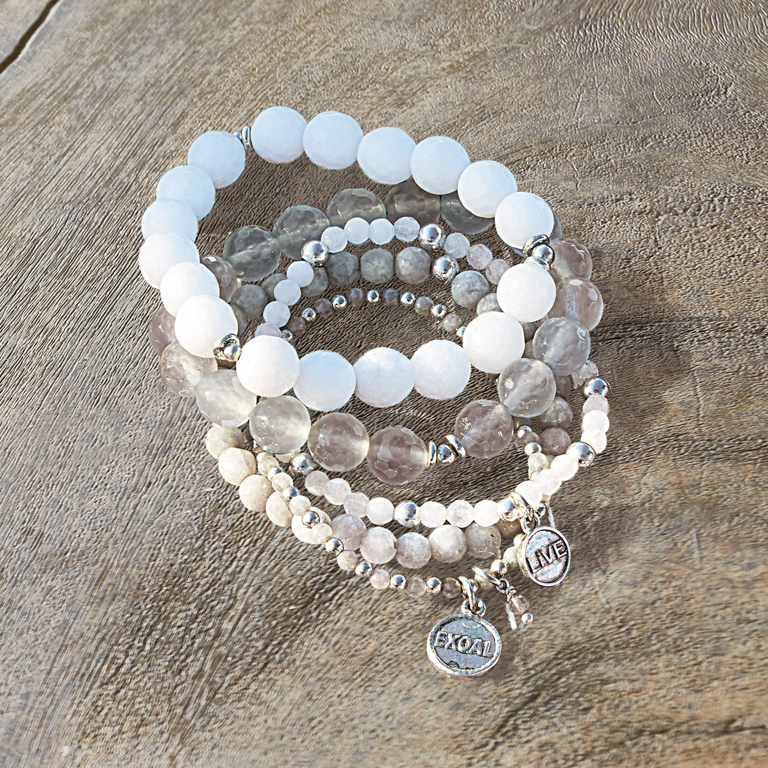 Set de 5 pulseras Chaim Conjunto de pulseras con piedras blancas y grises con dijes metálicos sobre fondo de madera
