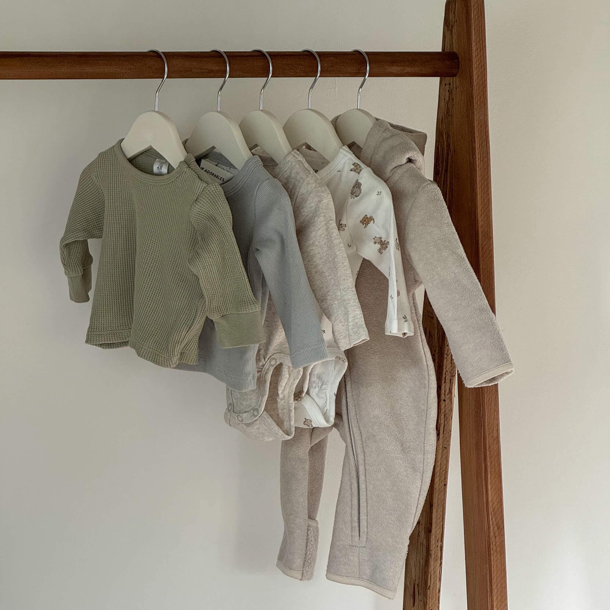 Conjunto de ropa infantil en tonos neutros colgado, tejidos suaves con estampados de osos