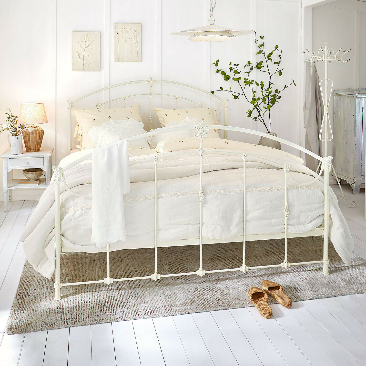 Cama Canefield Cama de metal blanca con ropa de cama crema y alfombra natural en dormitorio luminoso
