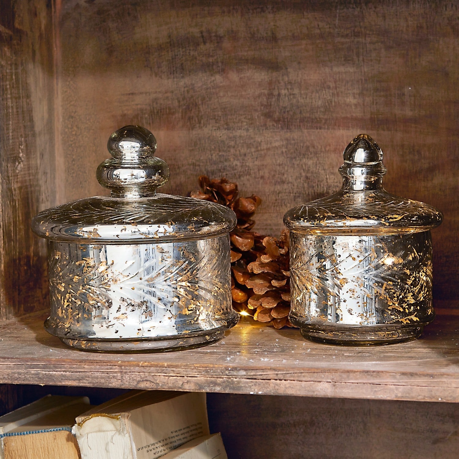 Set de 2 tarros de cristal Elexa Dos frascos de vidrio con tapas y decoraciones doradas en estante de madera con piñas