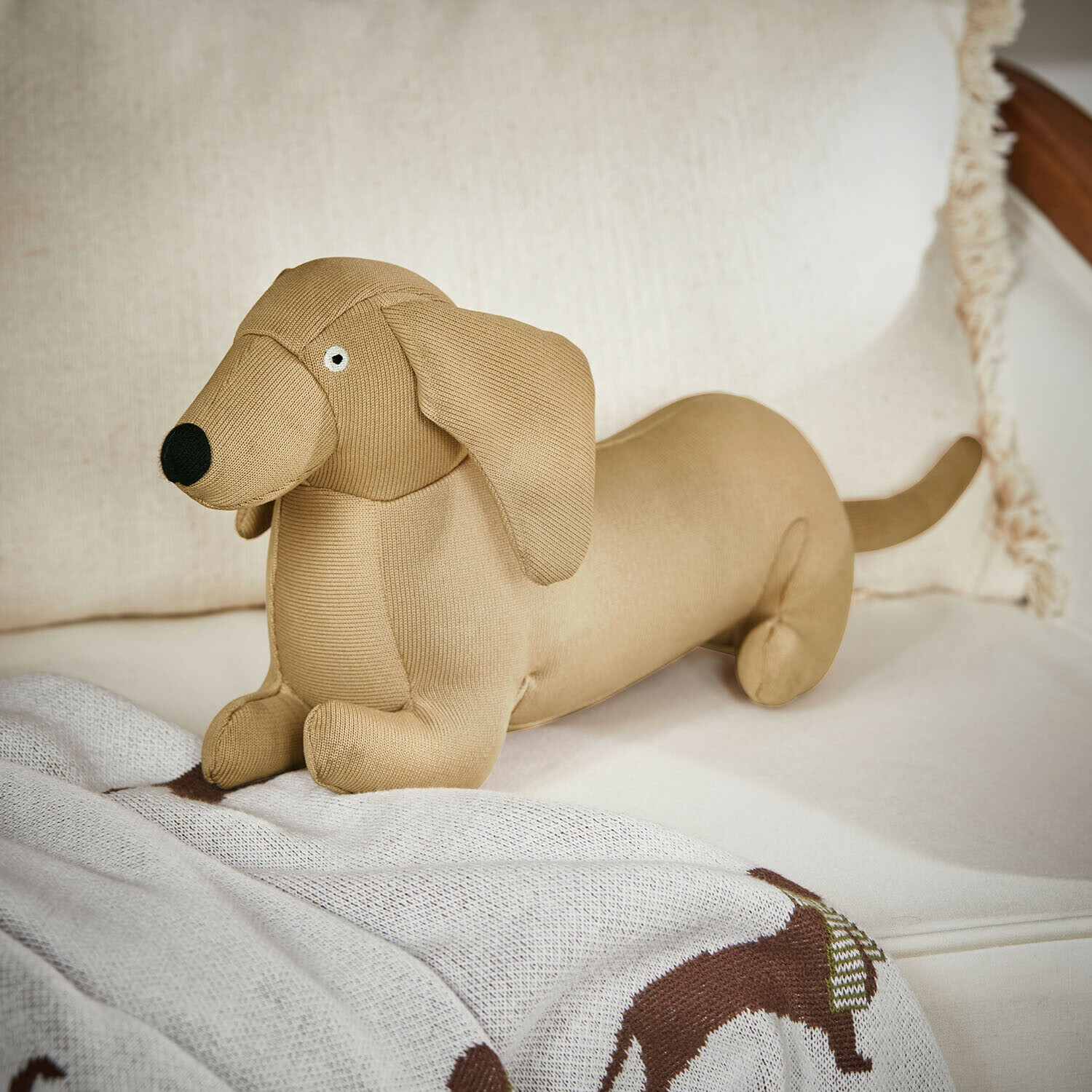 Juguete para mascotas Brisette Perrito salchicha de peluche beige de material suave sobre sofá, decoración y juguete infantil