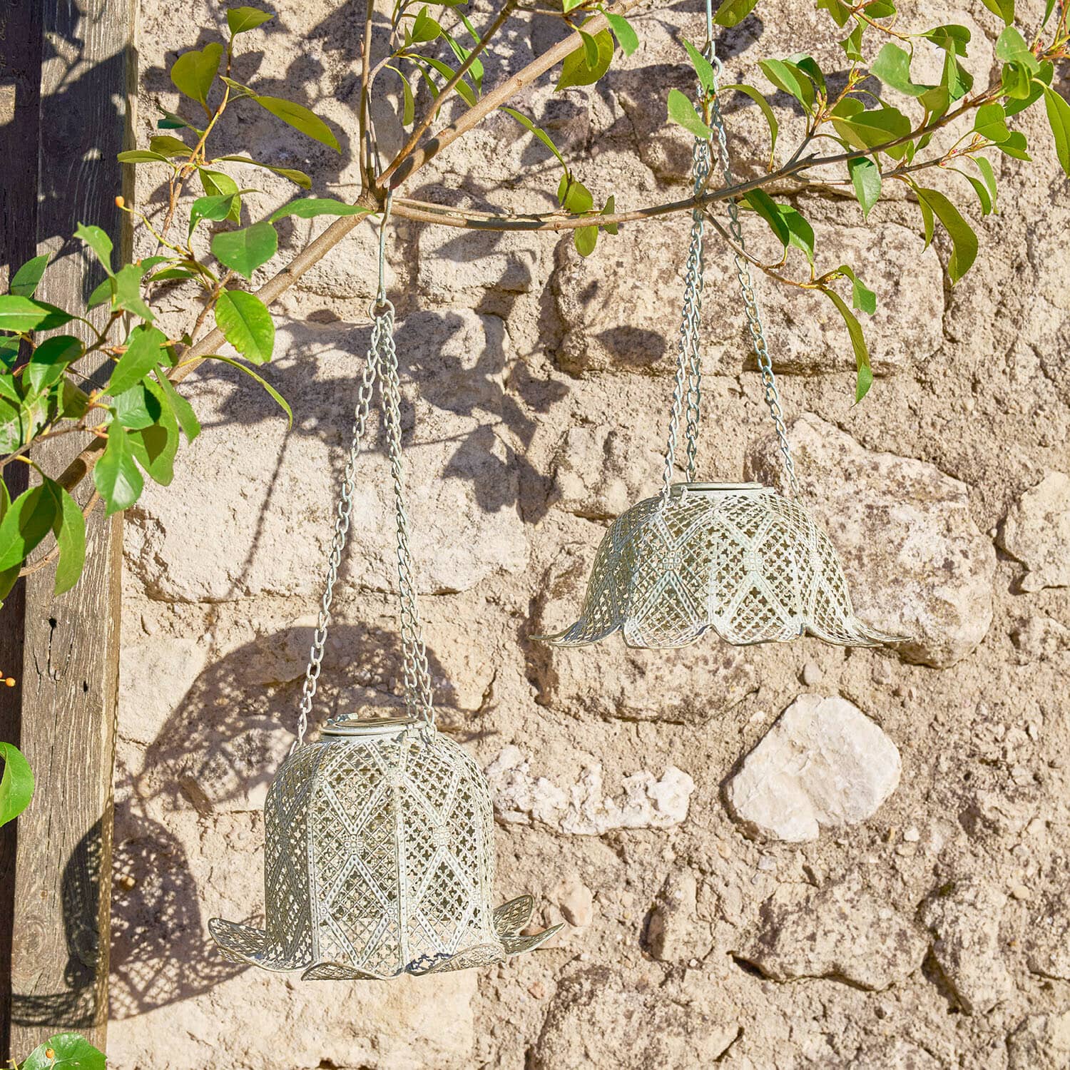 Set de 2 faroles solares Zuleya Dos faroles colgantes de metal en forma de campana color gris claro frente a una pared de piedra