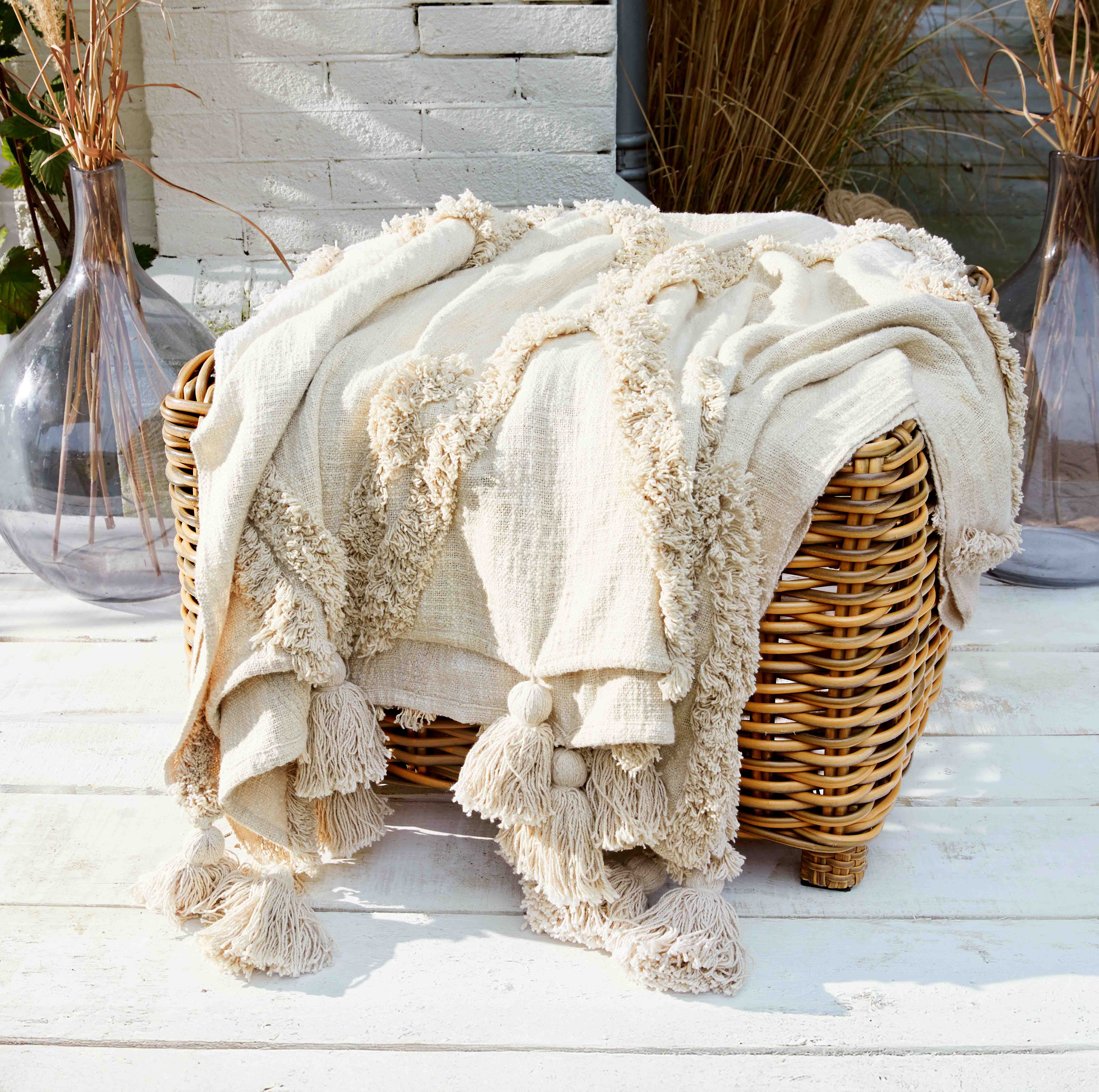 Manta crema con flecos de tela suave sobre sillón de mimbre, decoración interior y jardín