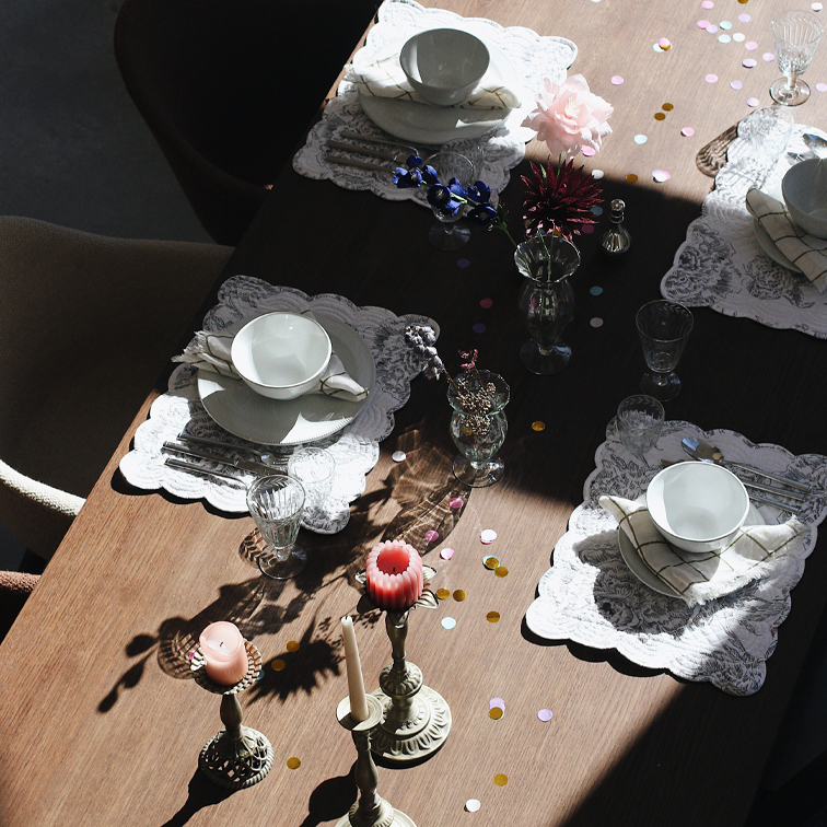 Mesa elegantemente puesta con vajilla blanca, vasos y velas sobre superficie de madera