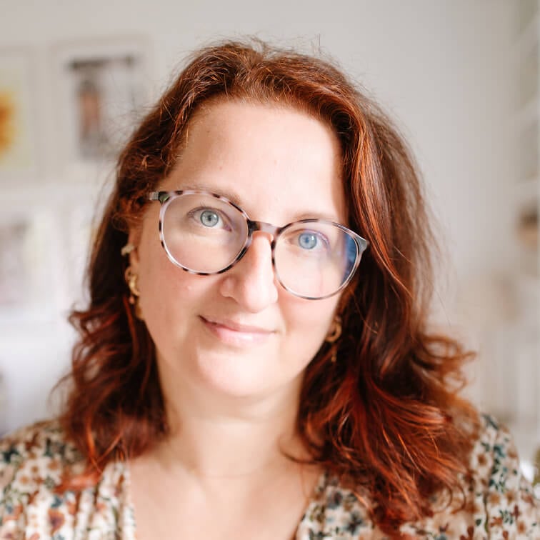 Retrato de mujer con cabello rojo y gafas en interior luminoso y desenfocado