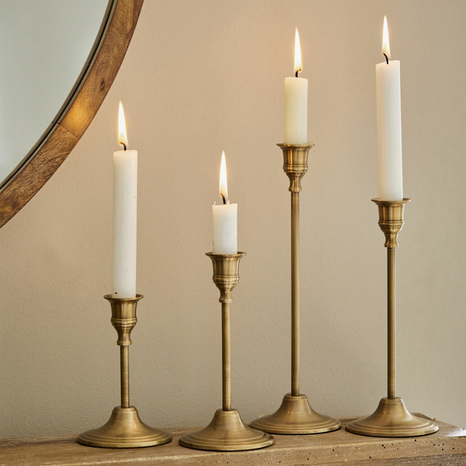 Set de 4 candeleros Namoris Conjunto de cuatro candelabros de latón con velas blancas sobre superficie de madera, decoración interior