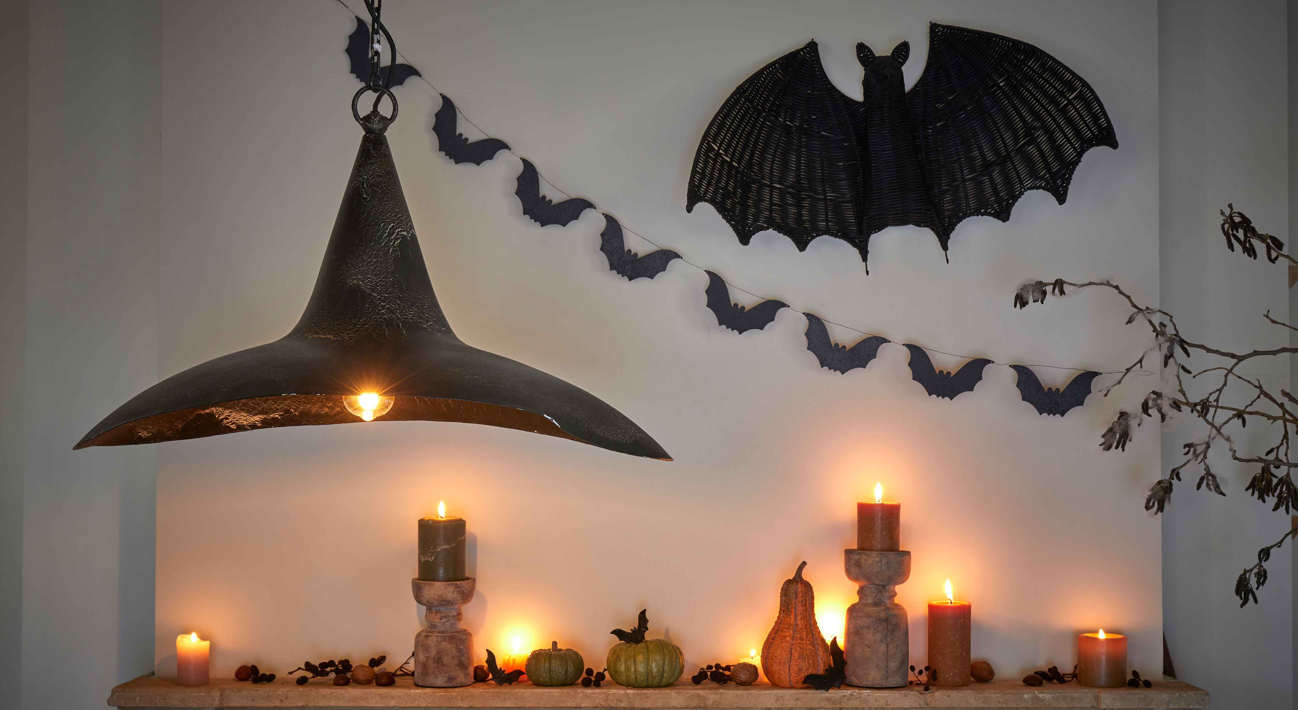 Decoración de Halloween con velas negras, calabazas y lámpara de metal negro en pared con murciélagos