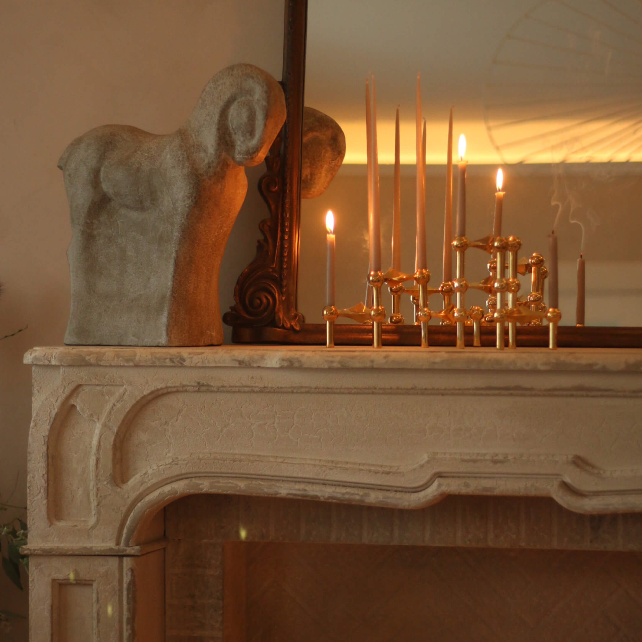 Escultura decorativa de carnero de piedra sobre chimenea con candelabro de latón y velas encendidas