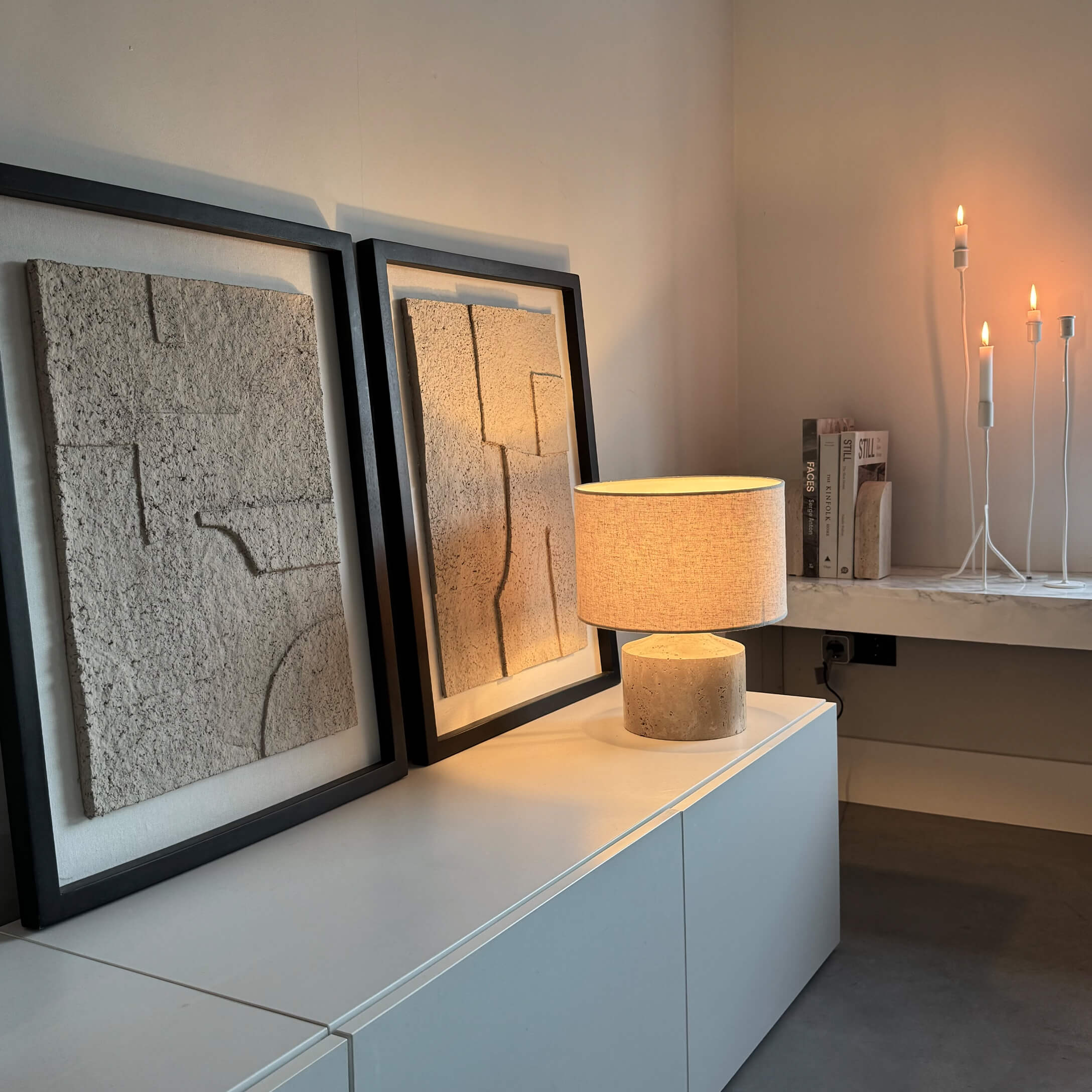 Lámpara de mesa moderna con pantalla beige y base de piedra sobre mueble blanco con decoración mural texturizada