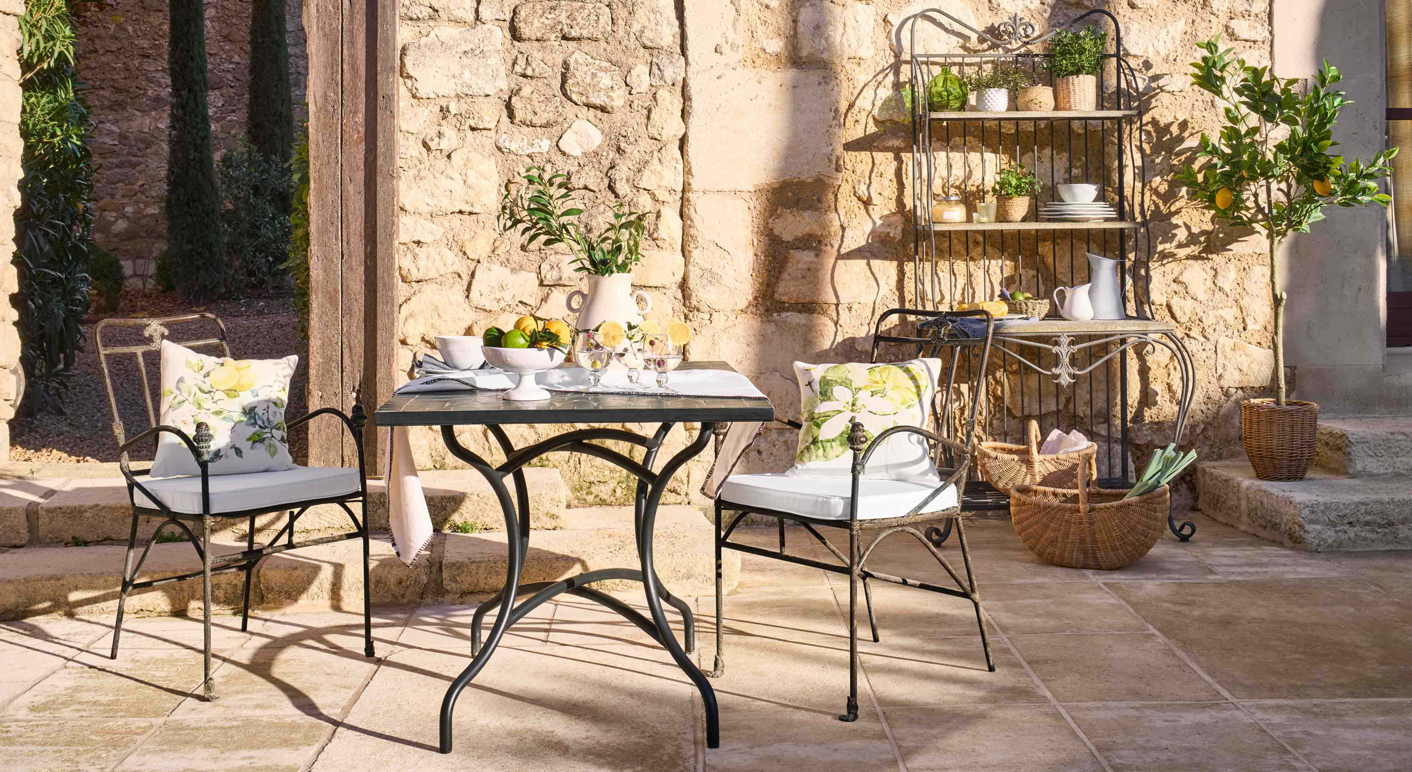 Mesa y sillas de metal con cojines florales en patio de piedra con decoración de jardín