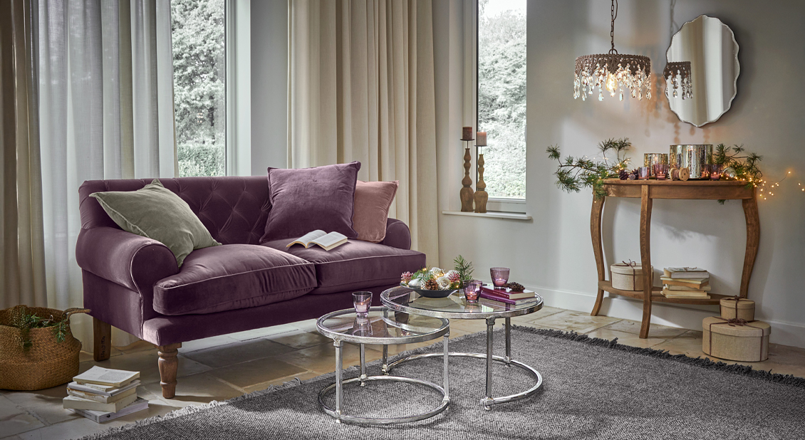 Sofá de terciopelo lila con cojines en salón acogedor con mesa decorativa y espejo