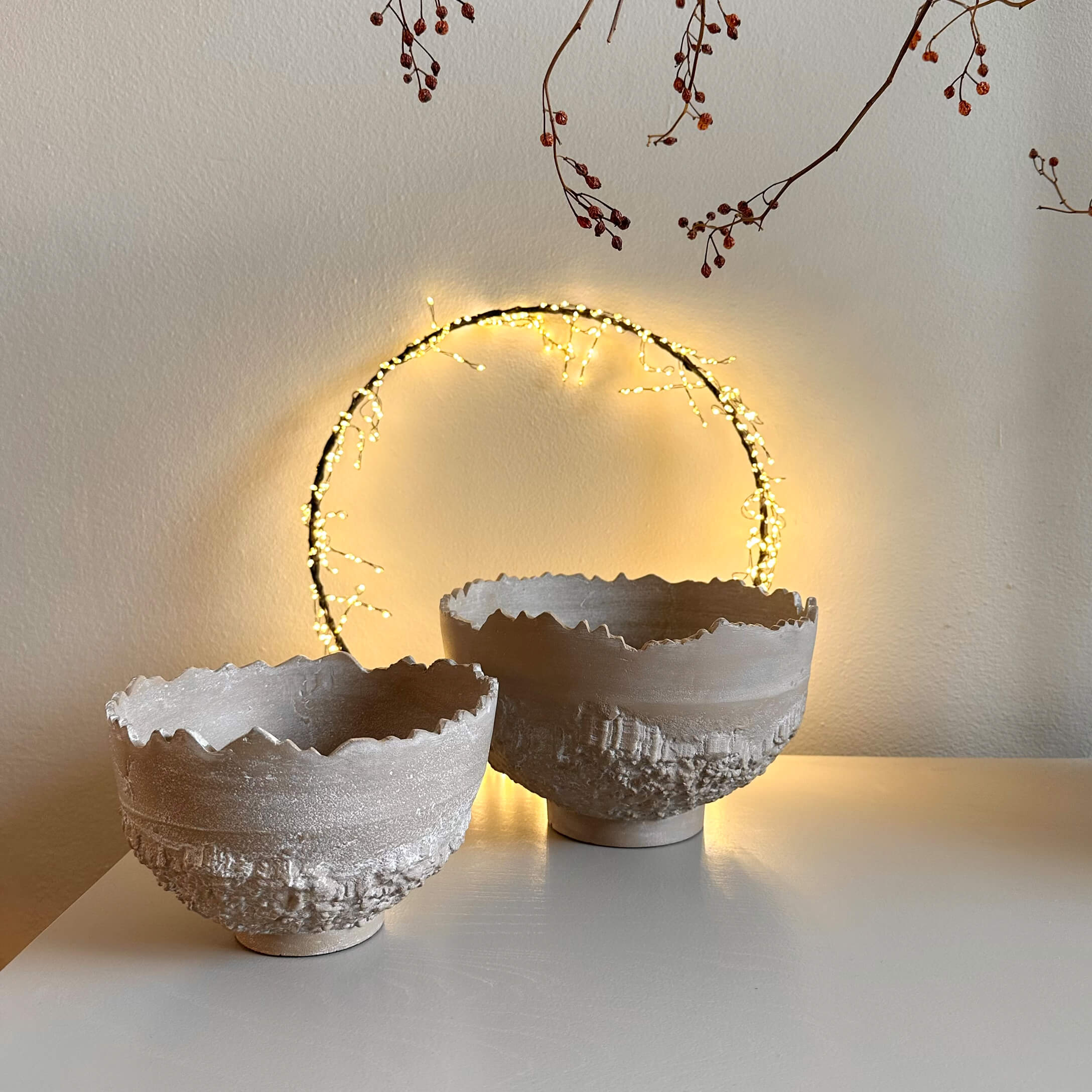 Dos cuencos decorativos de cerámica beige con textura rugosa y borde irregular sobre mesa blanca
