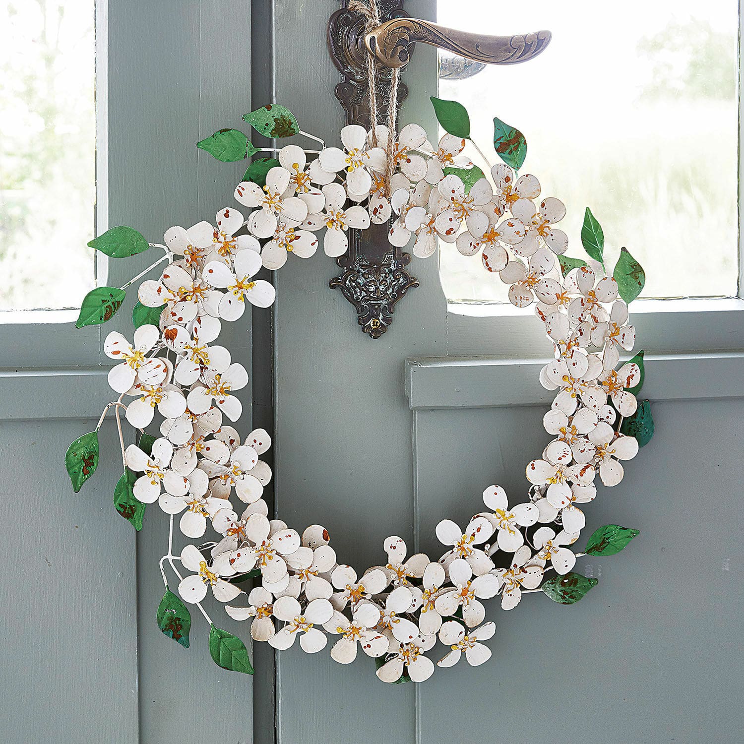 Corona Loanne Corona decorativa de metal blanco con flores y hojas verdes colgada en puerta gris