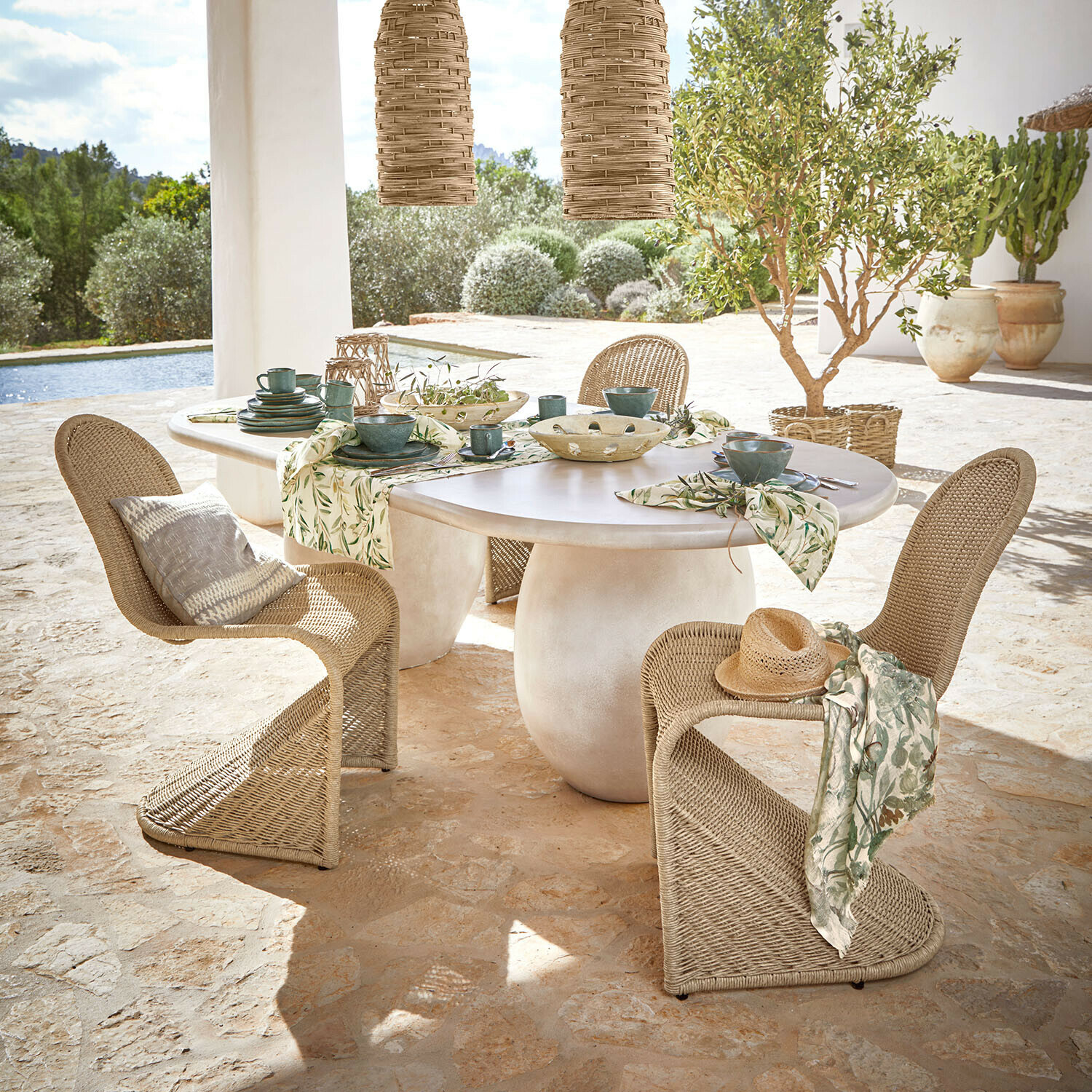 Mesa Arevalon Mesa ovalada con tablero blanco y sillas de mimbre natural en terraza con vistas al jardín