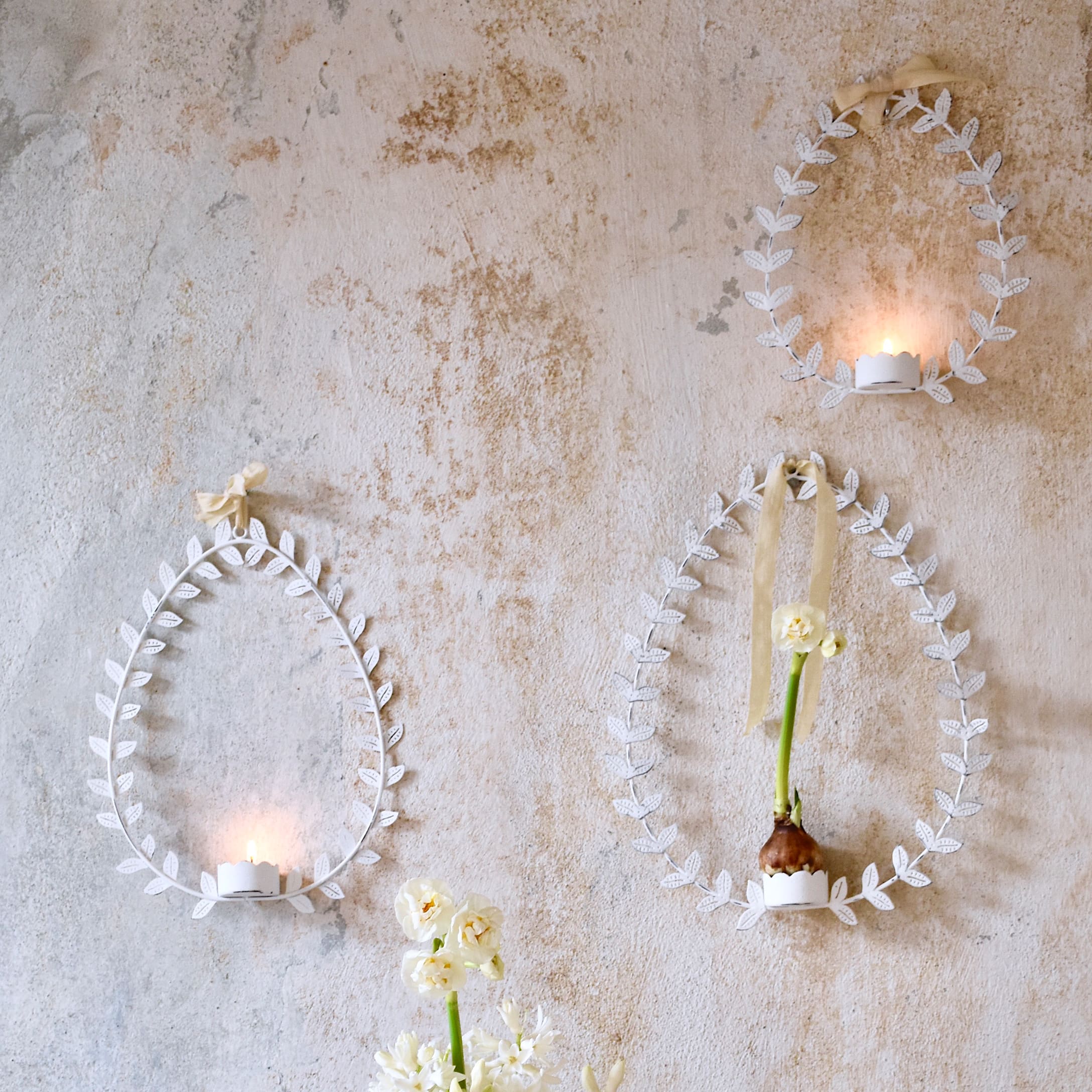 Marcos decorativos blancos de metal en forma de huevo con hojas, velas y flores en pared rústica