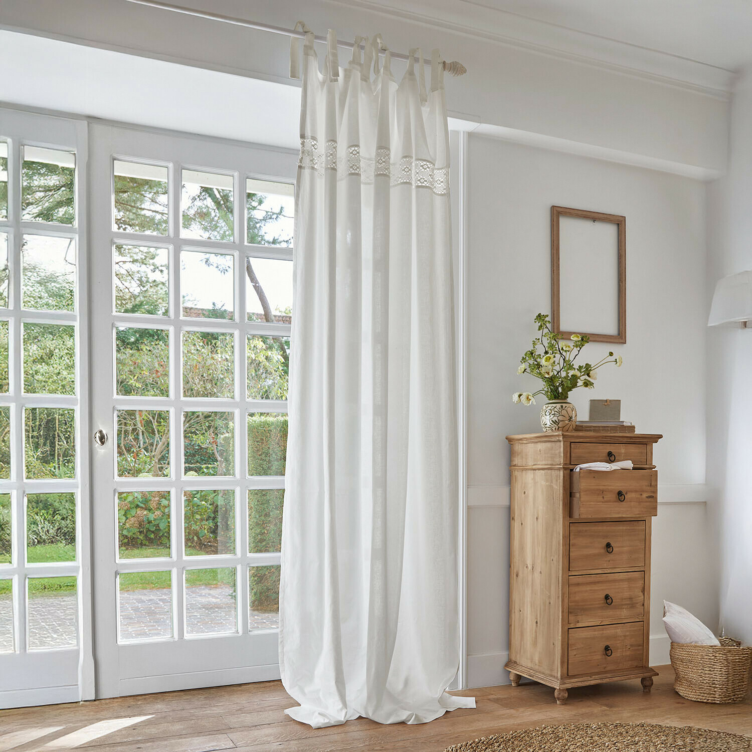 Cortina blanca de algodón con banda de encaje en habitación luminosa con cómoda de madera natural