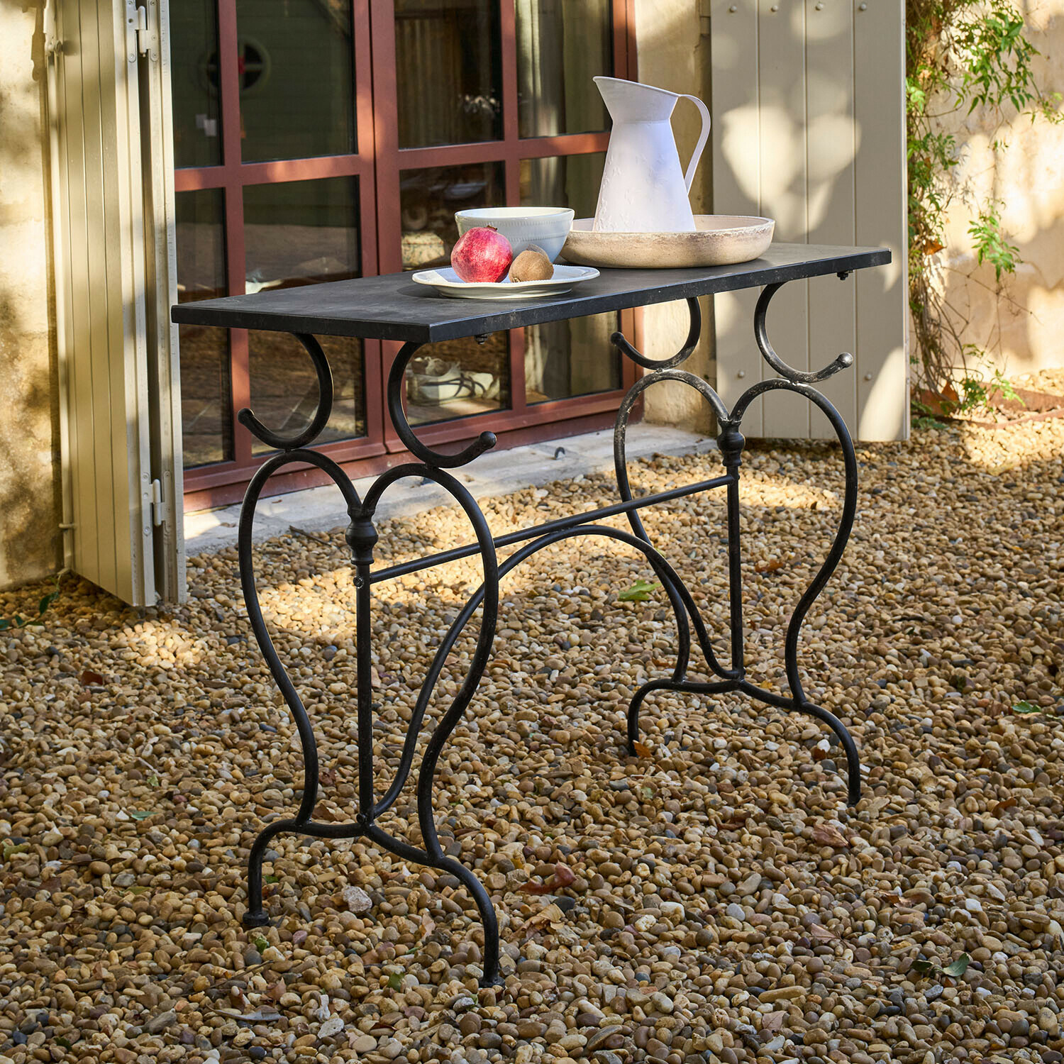 Mesa Cauvrel Mesa de jardín de metal negro con tablero rectangular sobre suelo de grava con decoraciones