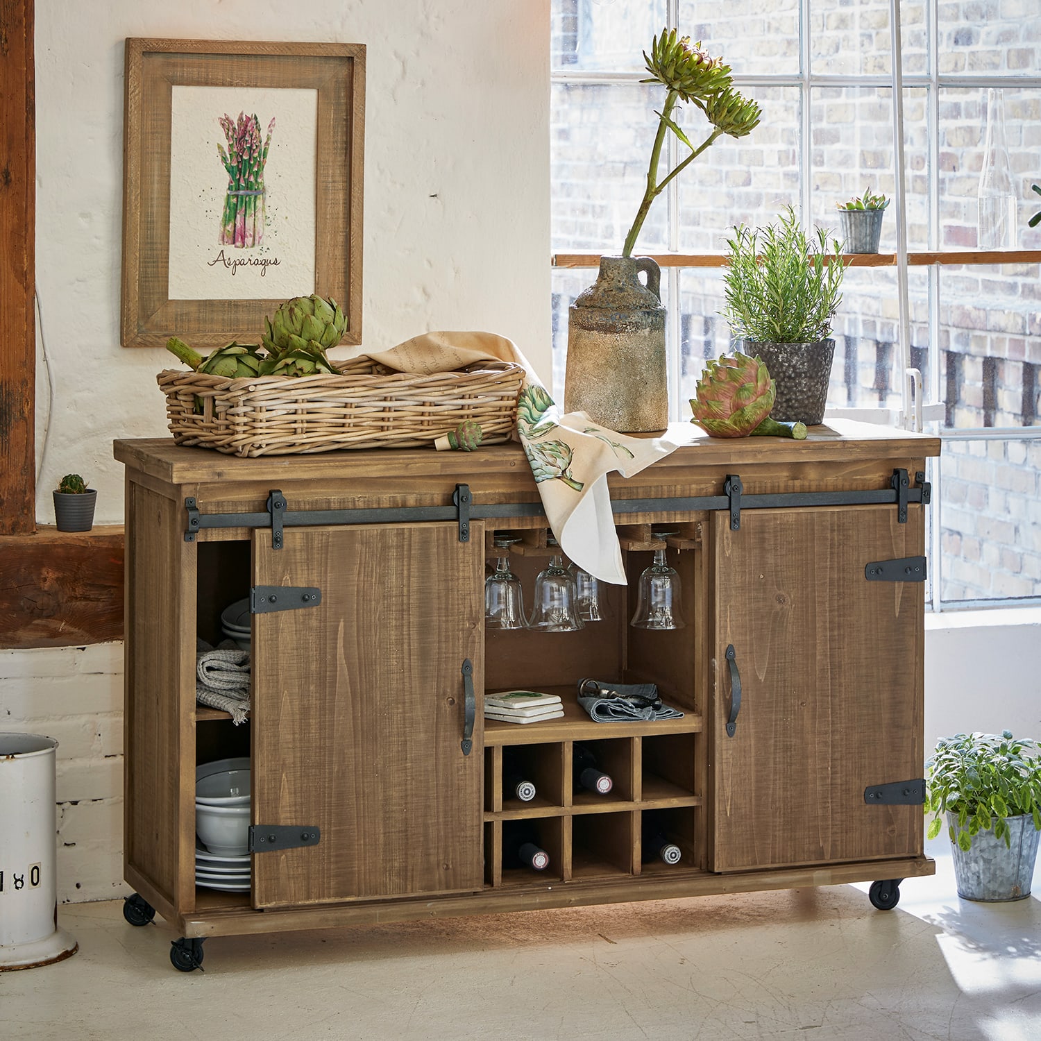 Aparador de madera con ruedas, espacio para vino y copas, decorado con plantas y cesta de verduras