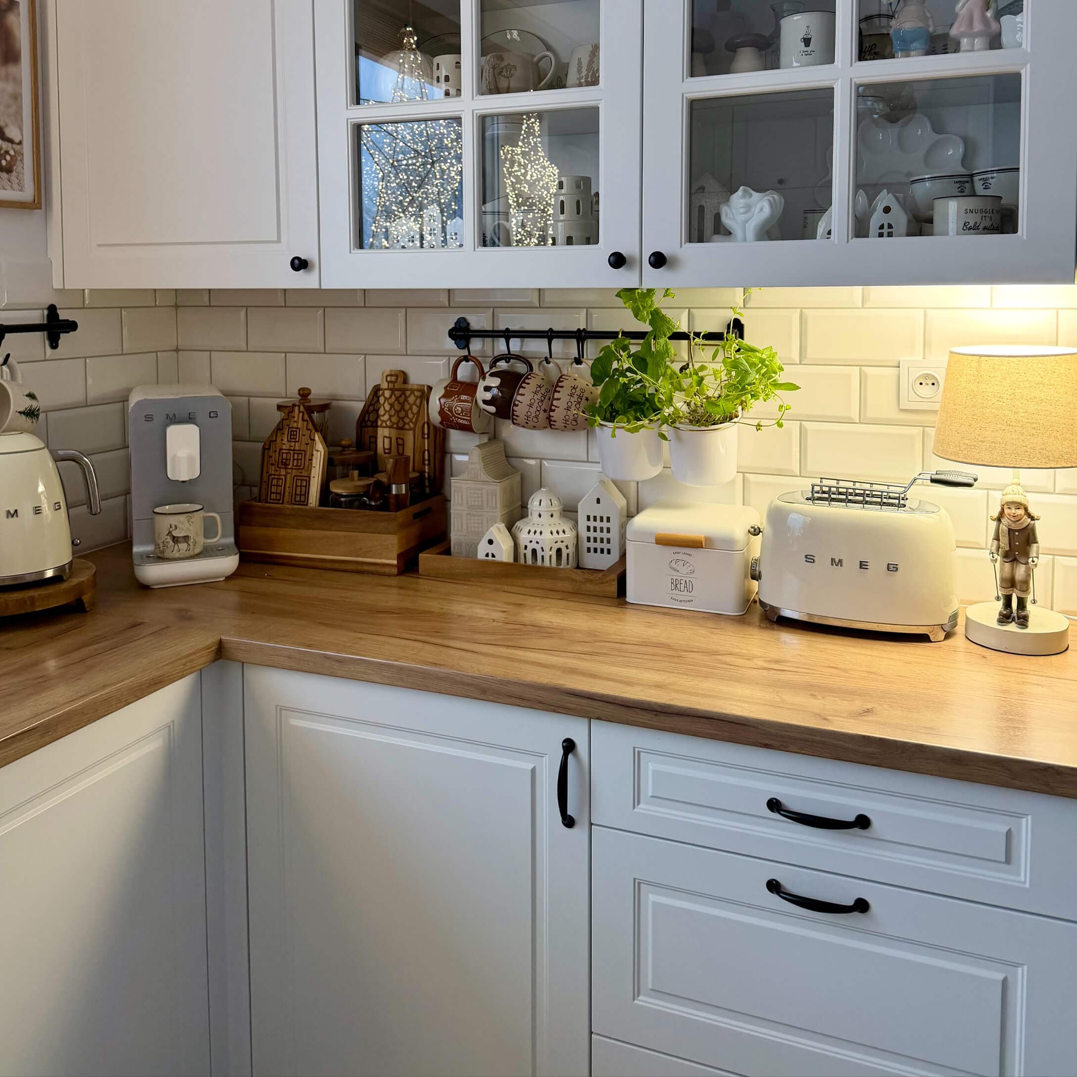 Cocina con armarios blancos, encimera de madera, electrodomésticos SMEG crema y decoraciones con plantas verdes