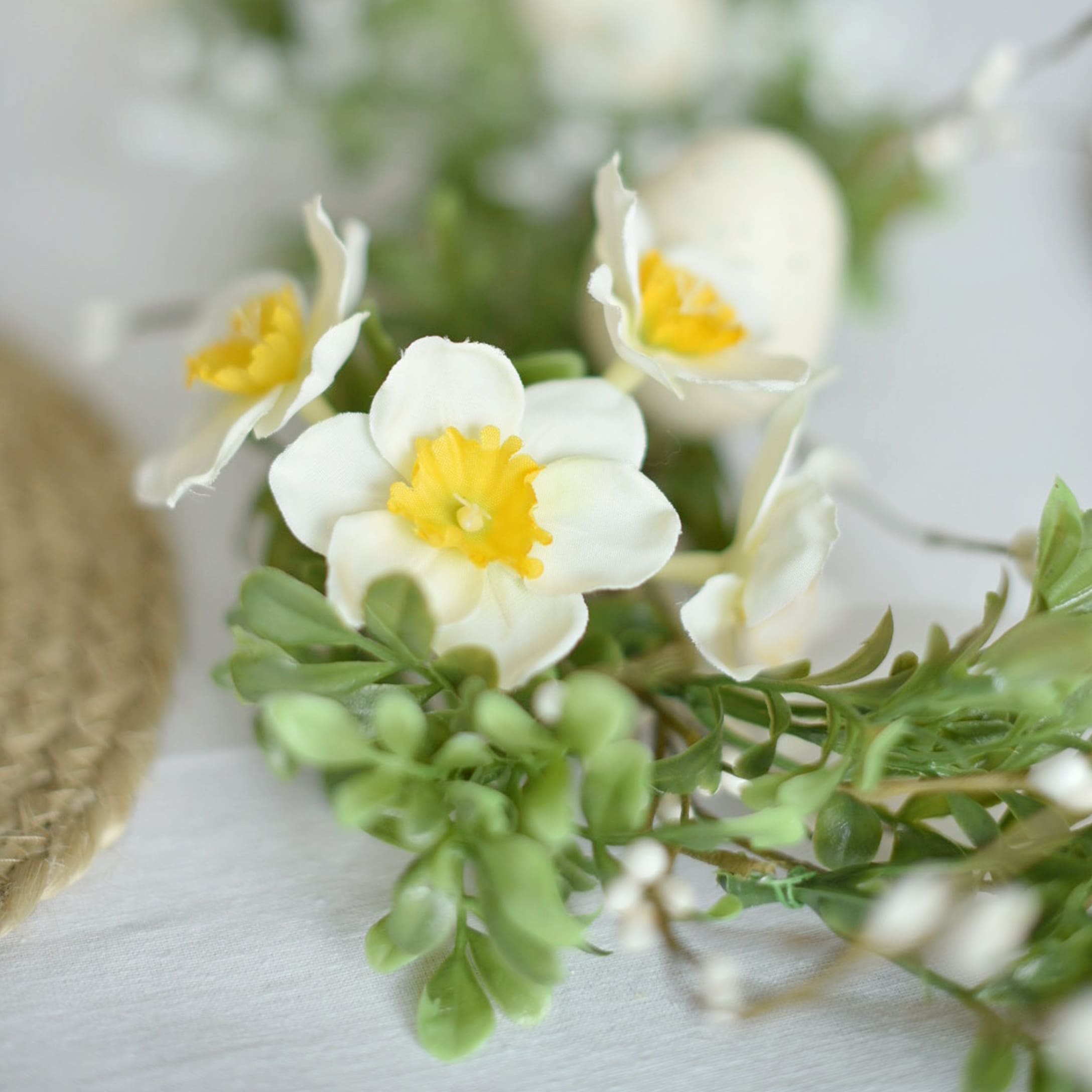 Corona decorativa con flores blancas y amarillas y hojas verdes sobre fondo claro
