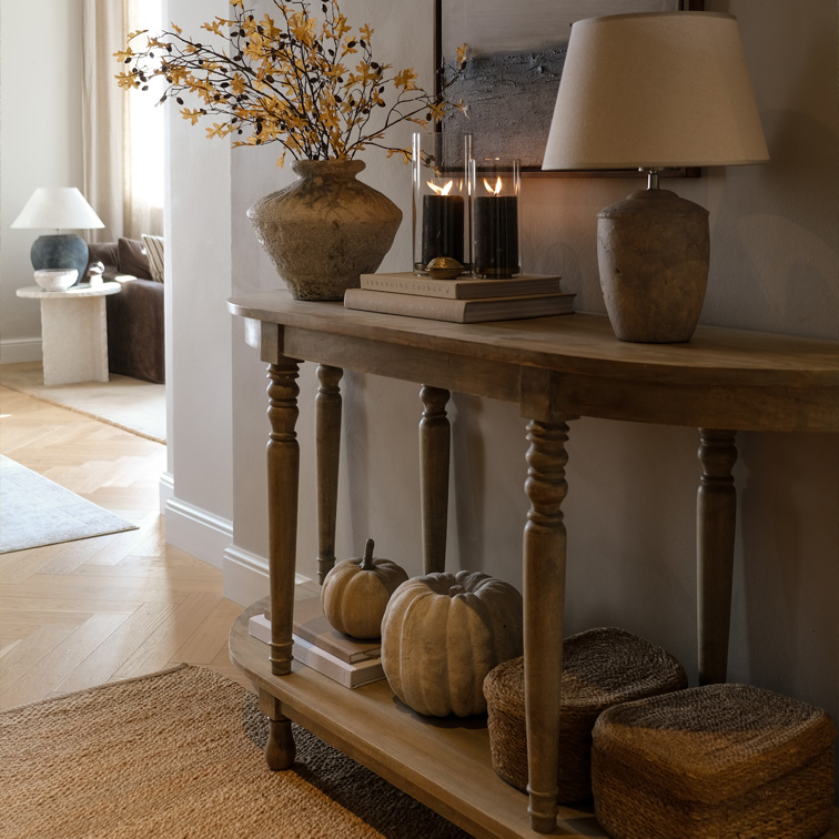 Consola de madera con decoración otoñal, lámpara y velas en salón acogedor con detalles naturales