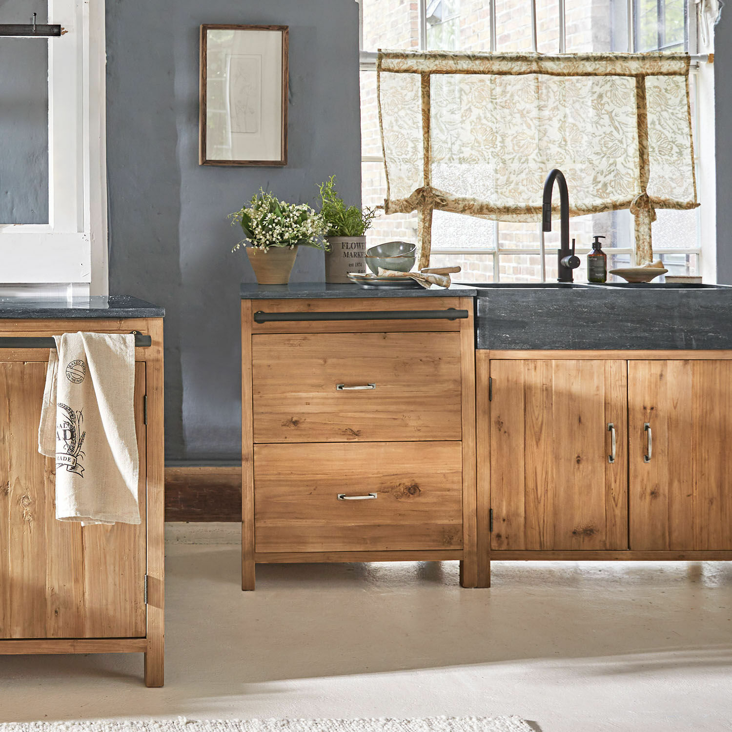 Armario bajo Sunnybrook Cocina con muebles de madera y encimera negra, decoración con plantas y cortinas con estampado floral