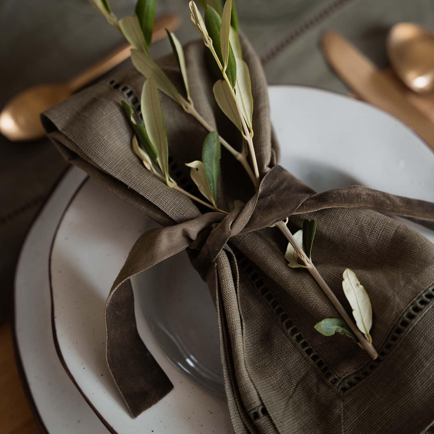 Servilleta de lino marrón con ramas verdes sobre plato blanco, decoración de mesa elegante