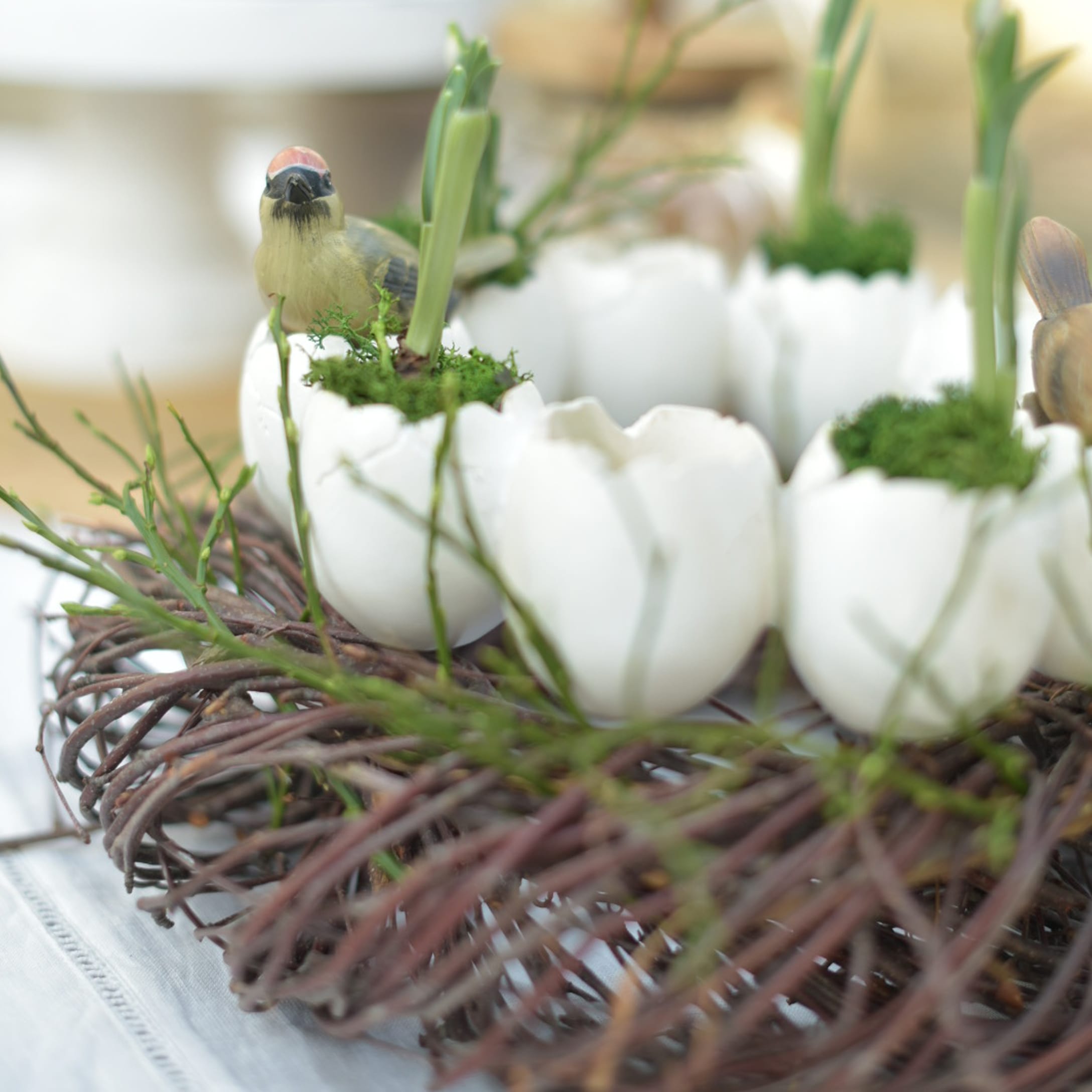 Corona decorativa con huevos de cerámica blanca, musgo verde y figuras de pájaros para Pascua