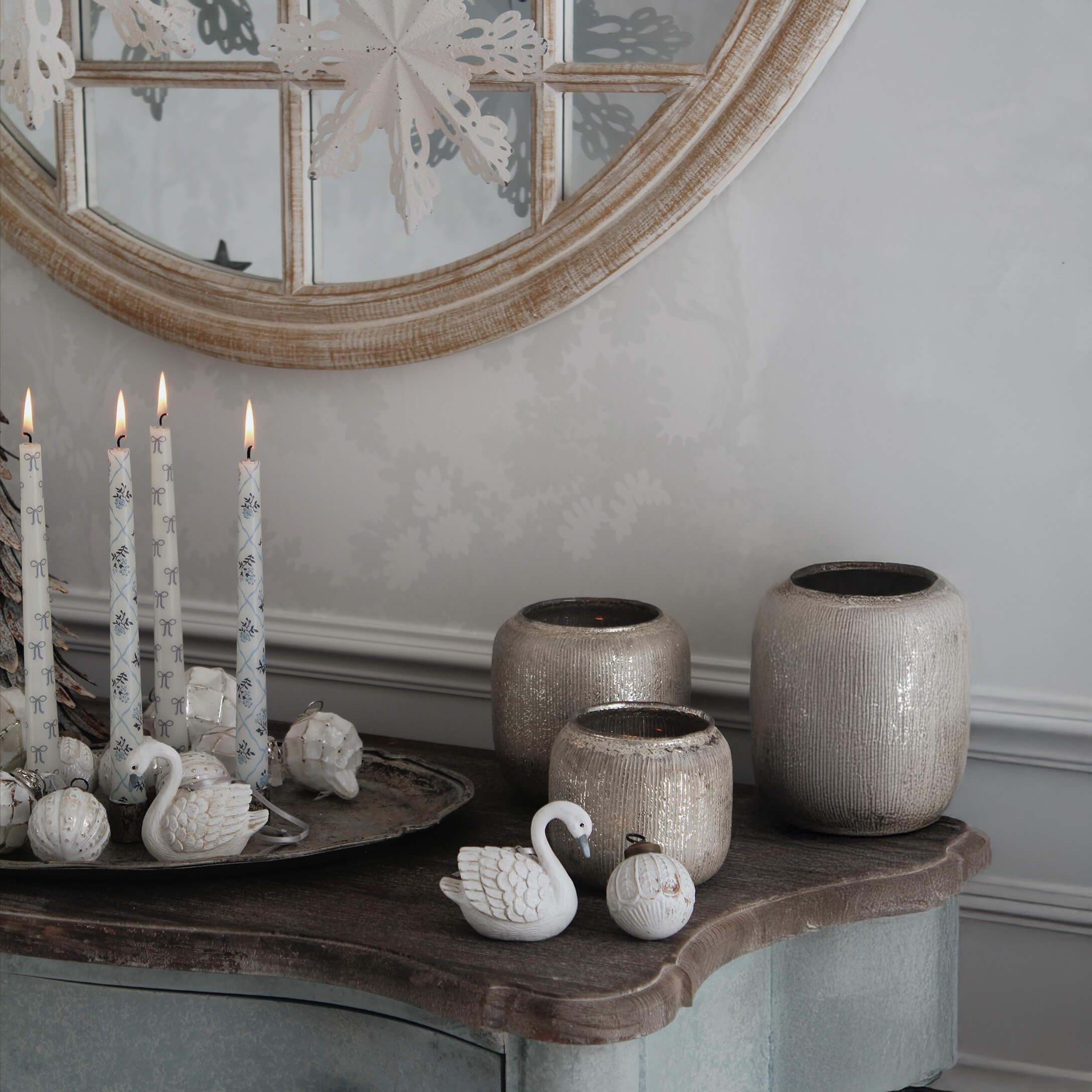 Velas blancas decorativas y jarrones de cerámica beige sobre mesa de madera con espejo redondo