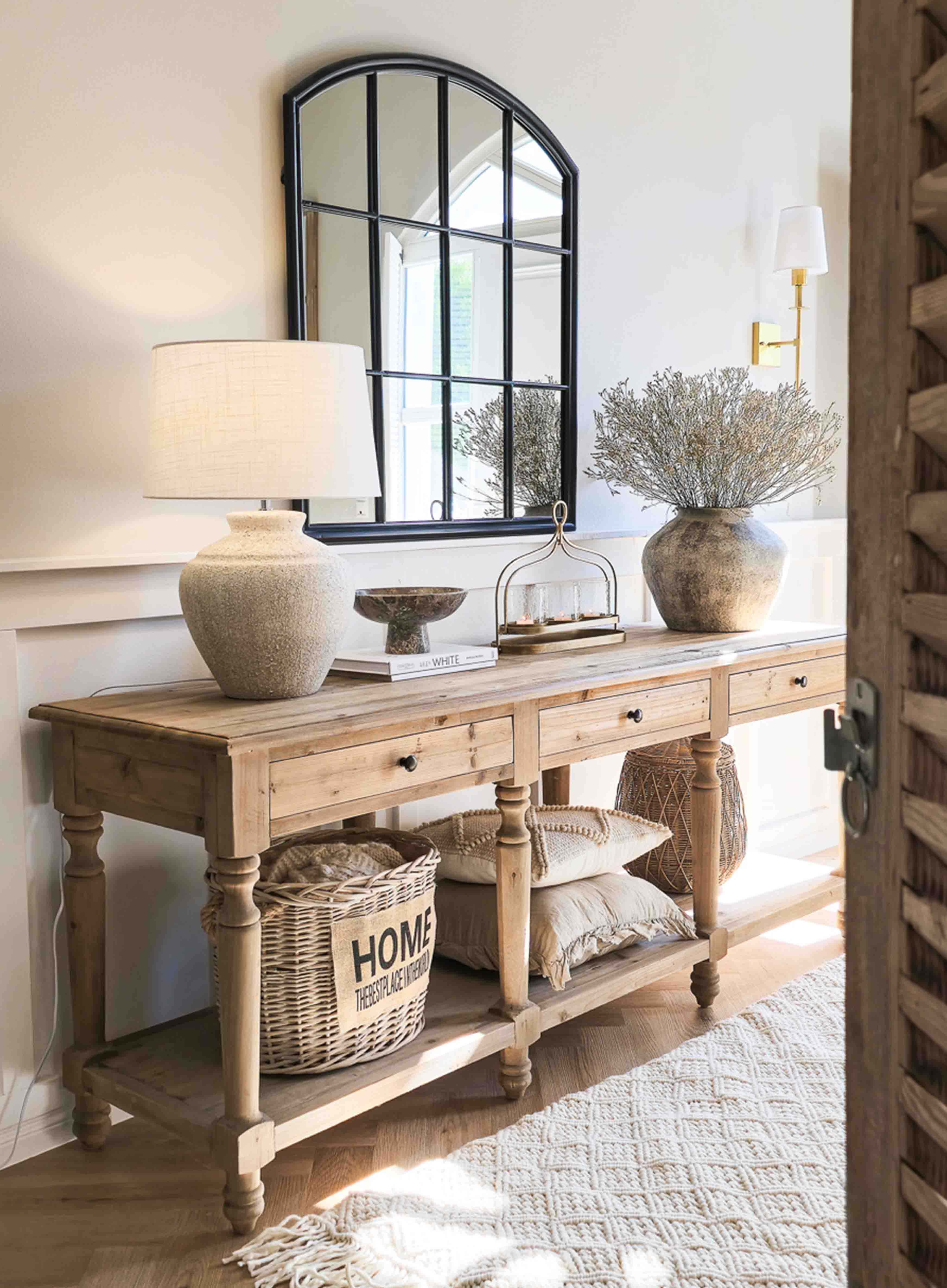 Consola de madera con lámpara de cerámica, espejo con marco negro y decoración rústica en interior luminoso