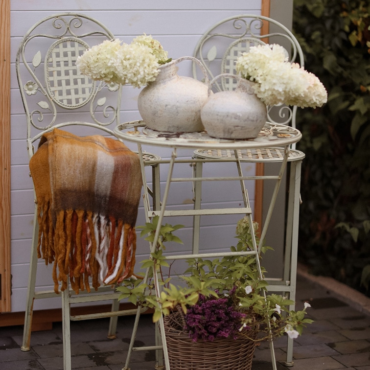 Mesa y dos sillas de metal vintage en color claro con jarrones decorativos y flores blancas