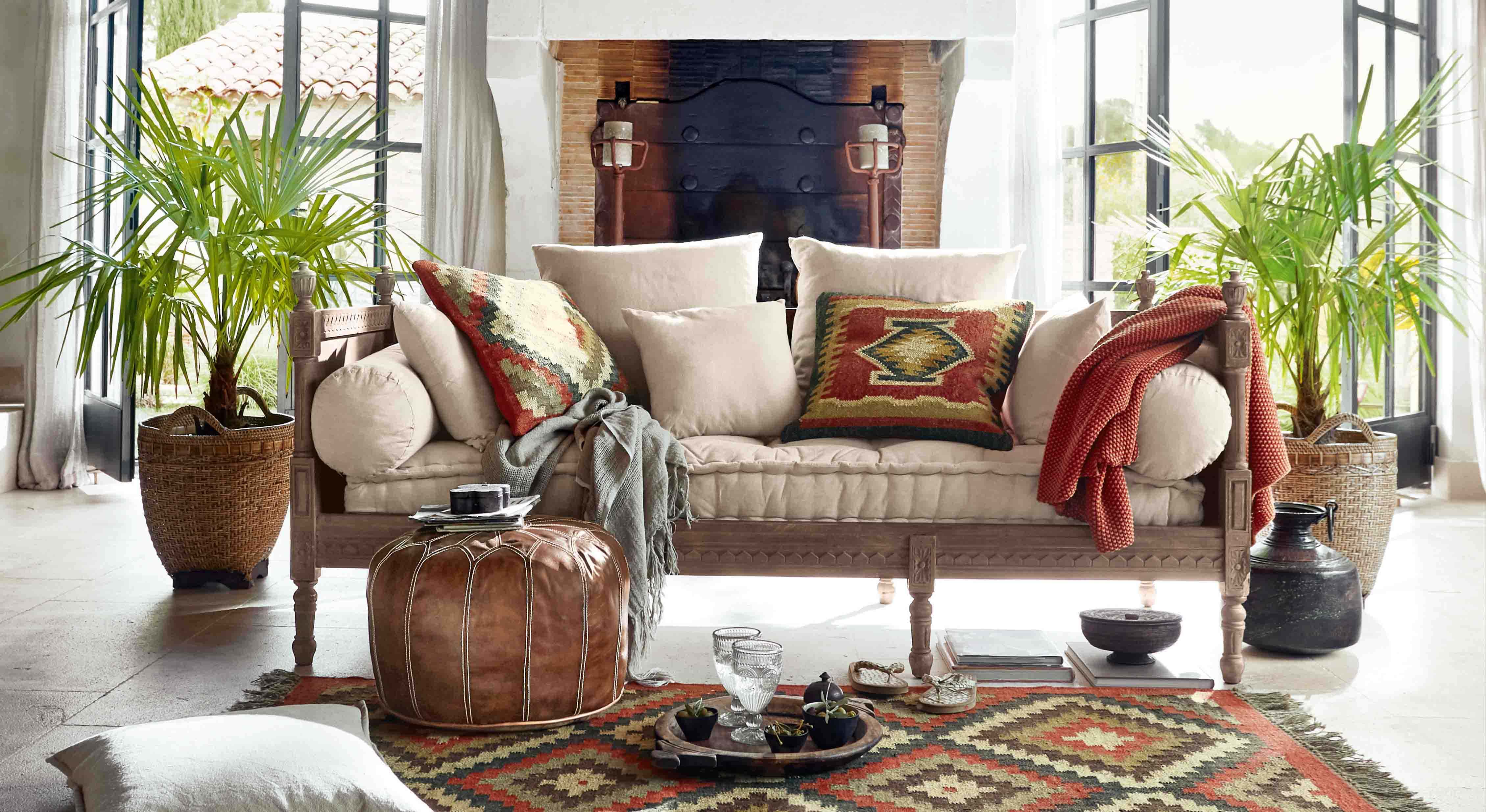 Sofá con tapizado beige claro y marco de madera, cojines coloridos y manta estilo bohemio en sala luminosa