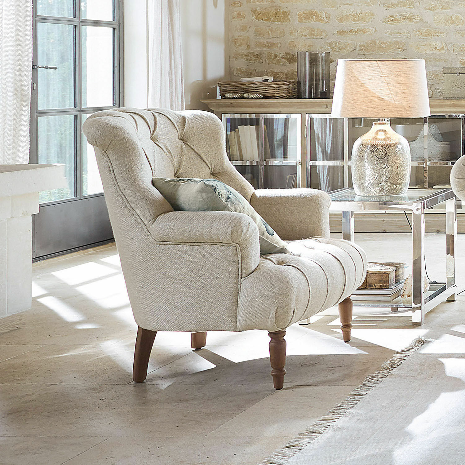 Sillón Parranquet Sillón tapizado beige con patas de madera en sala luminosa con lámpara y mesa auxiliar