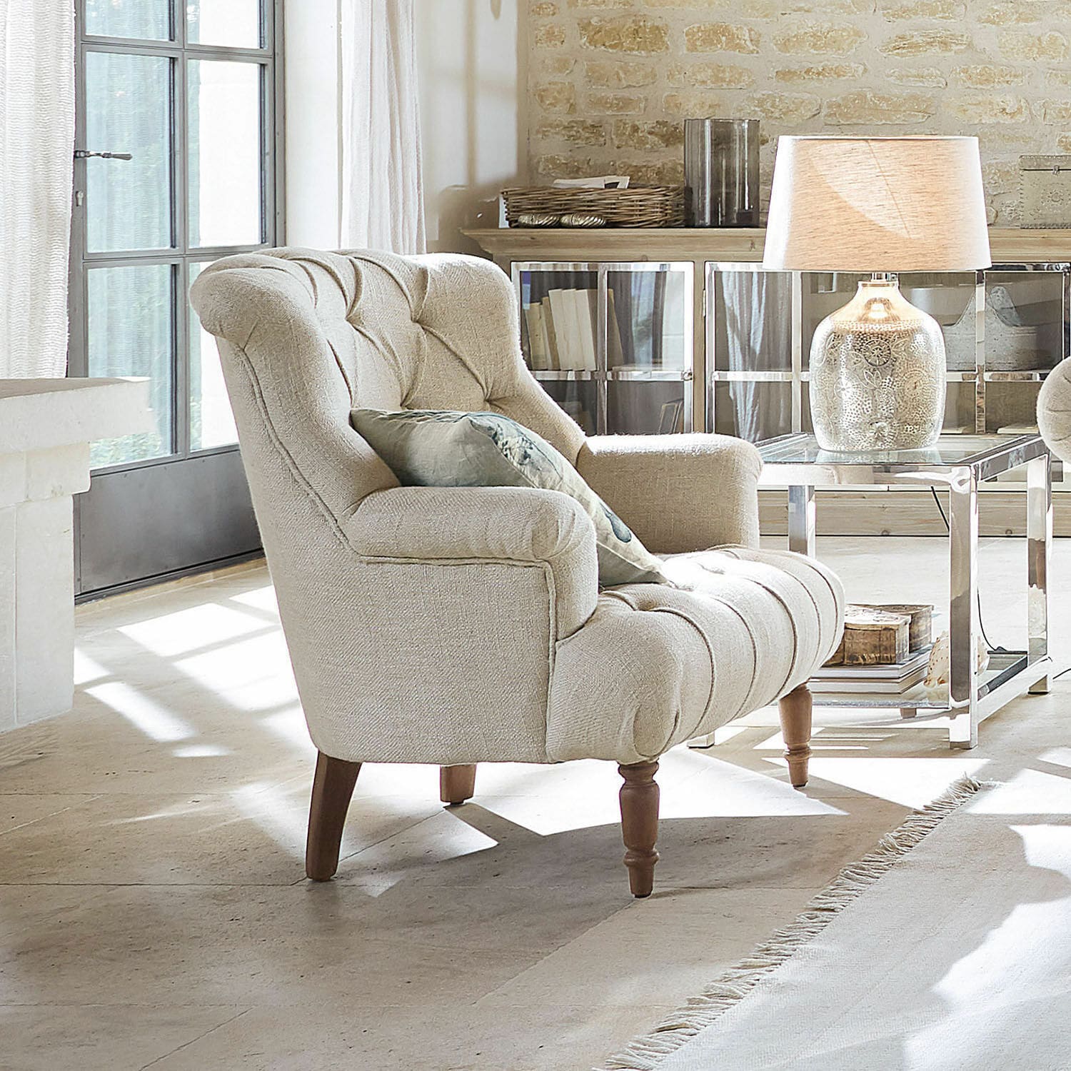Sillón Parranquet Sillón tapizado beige con patas de madera en sala luminosa con lámpara y mesa auxiliar