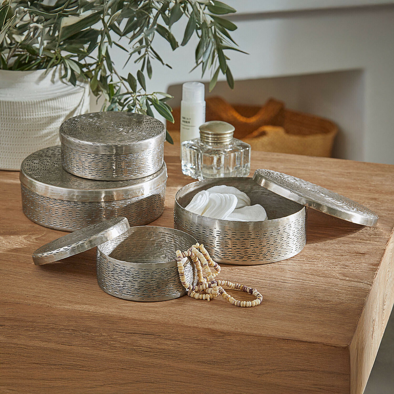Conjunto de tres recipientes redondos de metal plateado para guardar cosméticos y joyas sobre mesa de madera