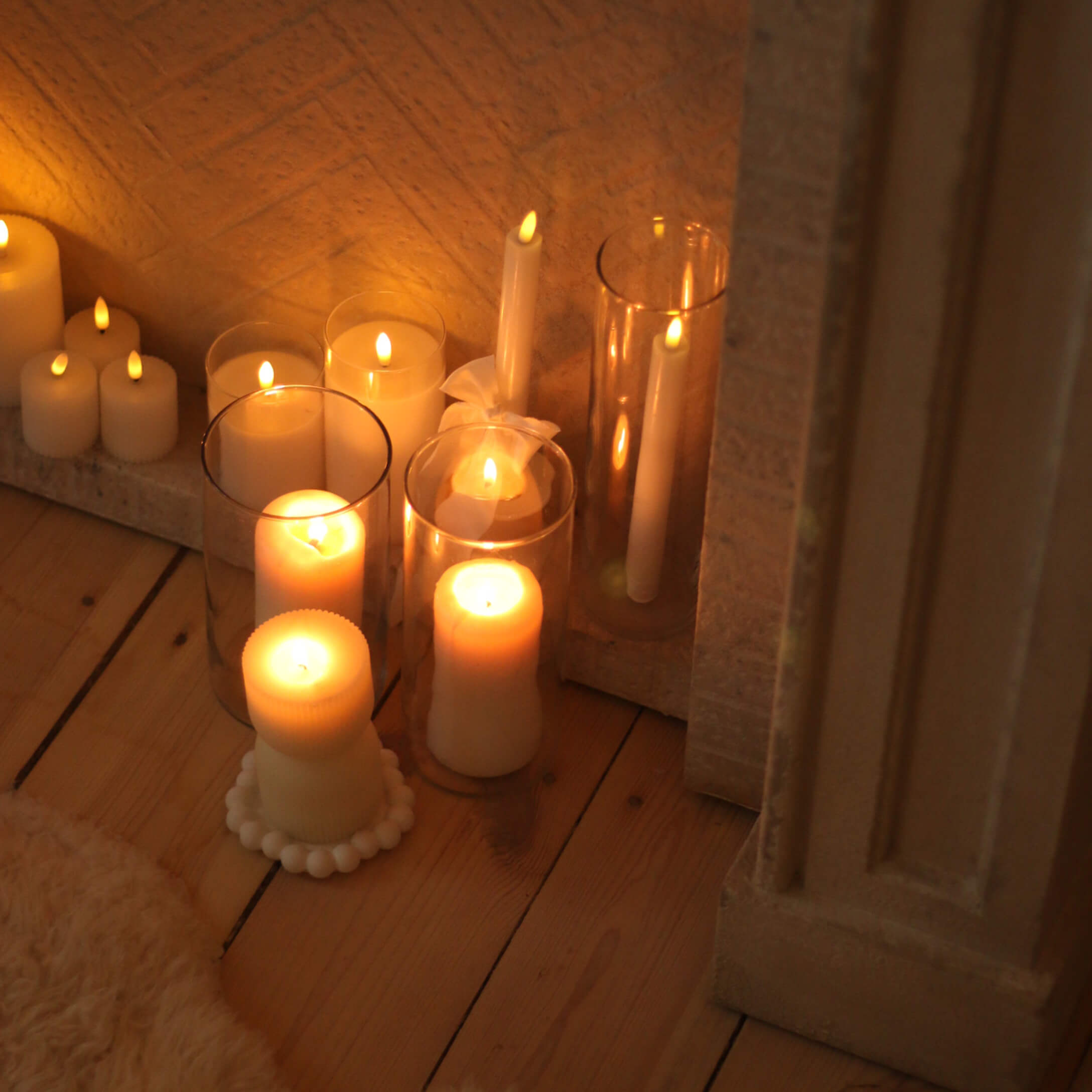 Conjunto de velas blancas de varios tamaños y formas sobre suelo de madera, decoración interior