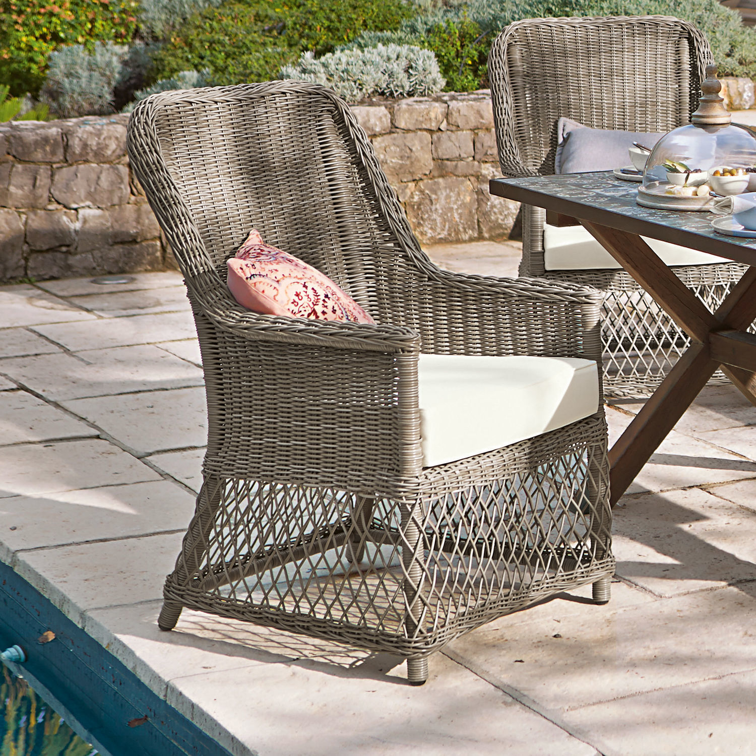 Sillón de ratán gris con cojín blanco y cojín decorativo rosa para exteriores