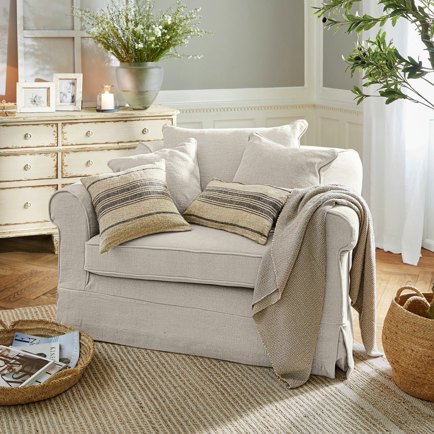 Sillón Folsom Sofá beige de tela con cojines a rayas y manta en sala acogedora con alfombra natural