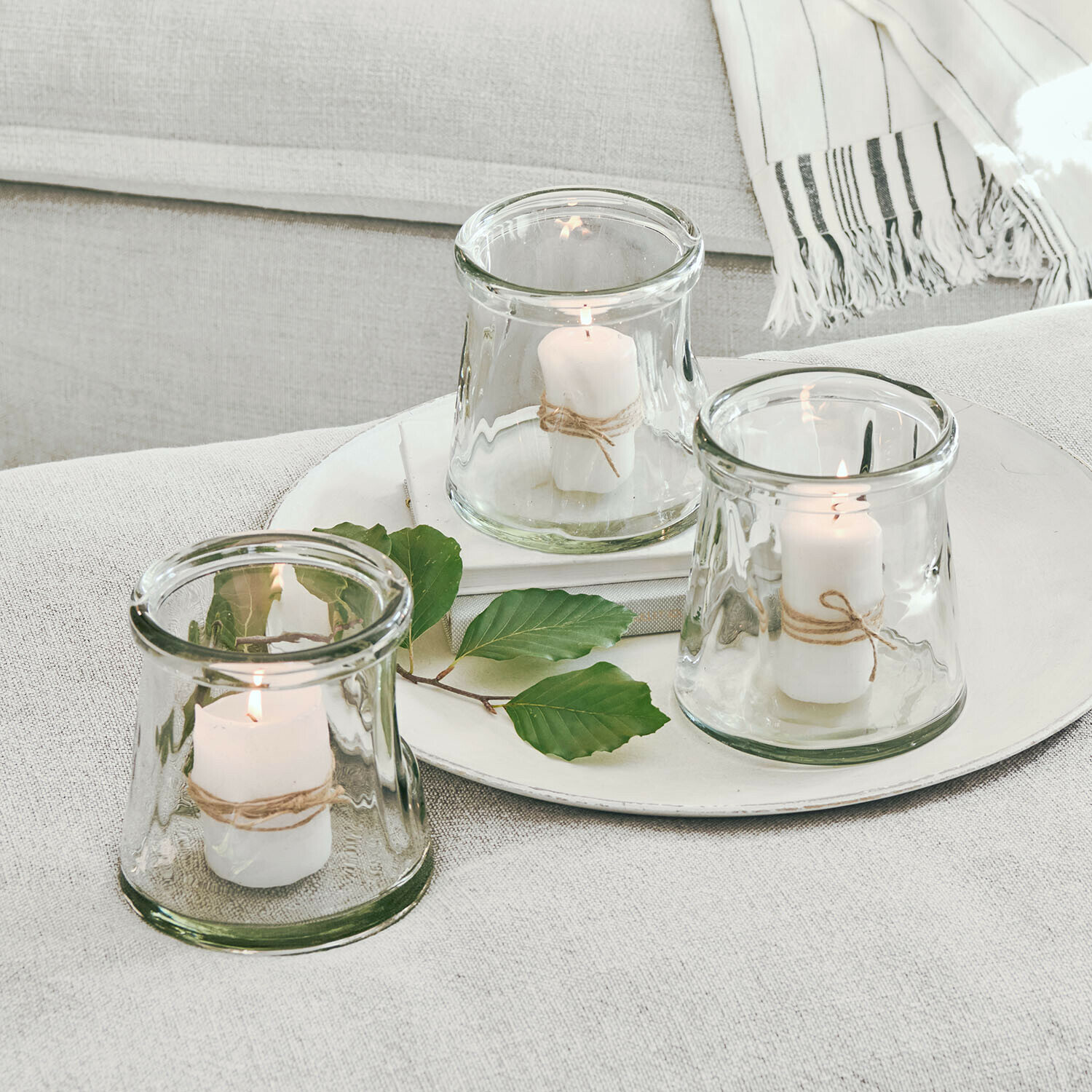 Conjunto de tres portavelas de vidrio con velas blancas y cuerda natural sobre fondo claro